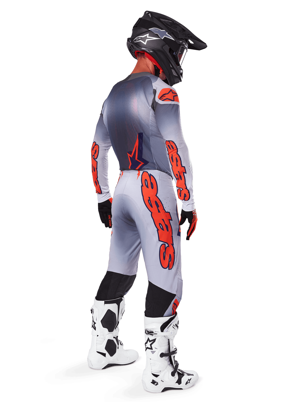Motocrossförare sedd snett bakifrån, bär 2025 Supertech Lipan-tröja och matchande byxor i grått och Orange Fluo, med framträdande orange Alpinestars-logotyper på ärmar och ben, kombinerat med en svart hjälm och vita stövlar, koordinerad outfit på proffsnivå för terrängkörning
