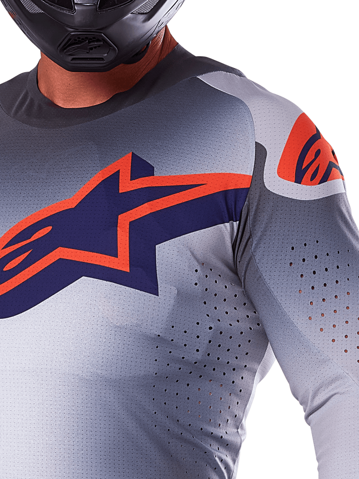Närbild av en förare i Alpinestars 2025 Supertech Lipan Jersey, motocrosströja i grått och neonorange, med en stor orange Alpinestars-logotyp på bröstet, laserskurna ventilationshål och svart hjälm, professionell racingutrustning.