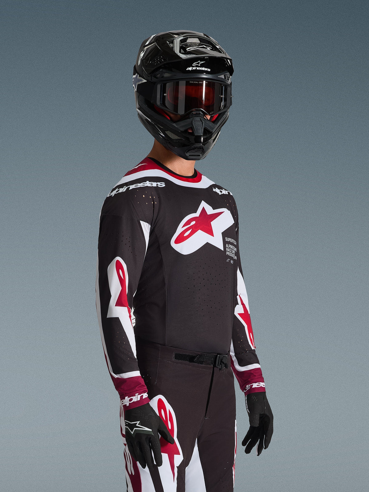 Alpinestars 2026 Supertech AFD Vista tröja, motocrossförare i komplett racingutrustning, svart tröja med röda och vita detaljer, stor logotyp på bröstet, laserskurna perforeringar, bärs med matchande byxor, svart hjälm och röda goggles, koordinerad outfit för terrängkörning