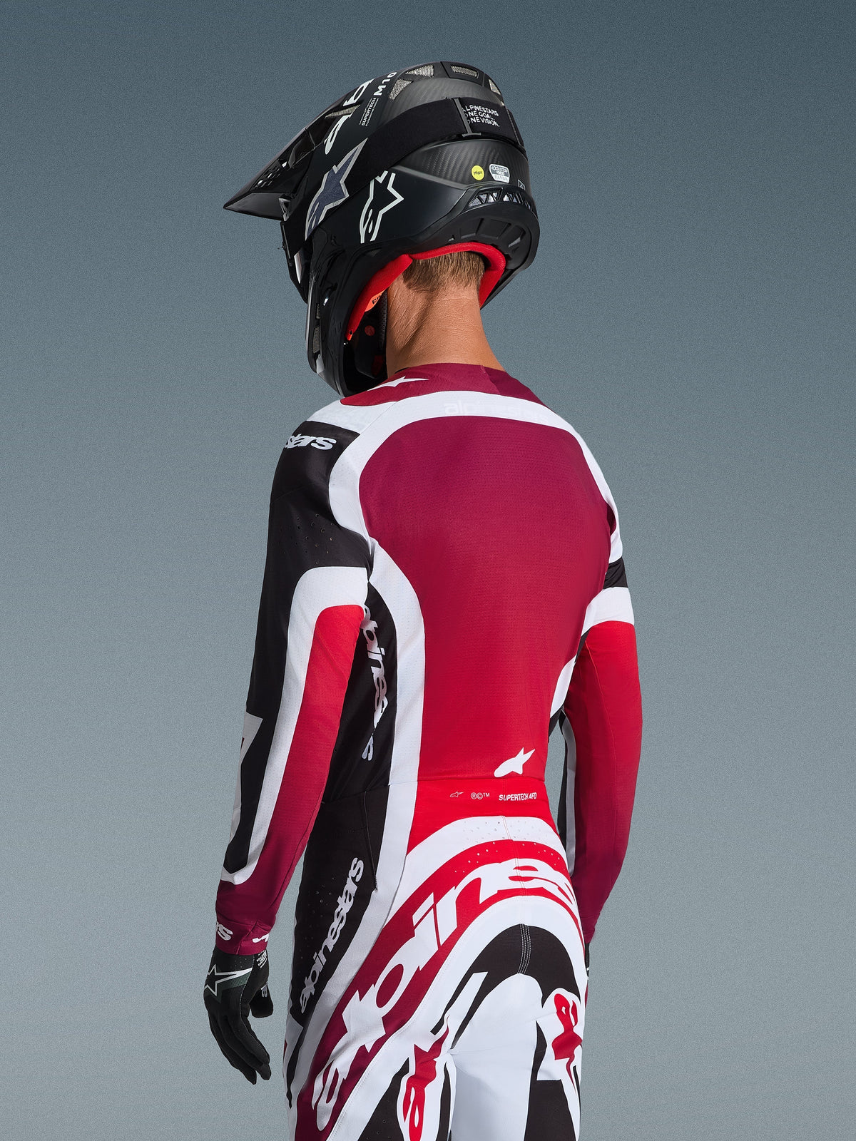 Alpinestars 2026 Supertech AFD Vista utrustningsset, vy bakifrån på en motocrossförare i svarta, röda och vita racingkläder, tröja med mörkröd ryggpanel och atletisk passform, matchande byxor med framträdande Alpinestars-logotyp, svart hjälm och handskar, professionell motocrossoutfit