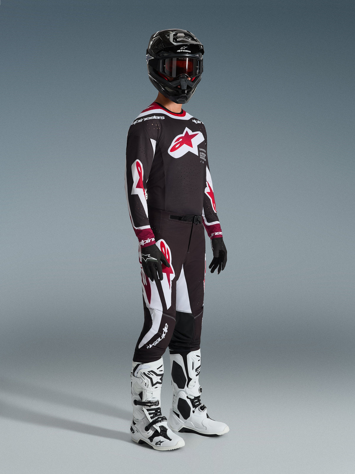 Alpinestars 2026 Supertech AFD Vista utrustningsset, motocrossförare i komplett racingutrustning, svart tröja med stor röd stjärnlogotyp på bröstet, matchande svarta byxor med röda och vita detaljer, vita och svarta motocross-stövlar, svart hjälm med röda goggles, professionell motocross-racingoutfit