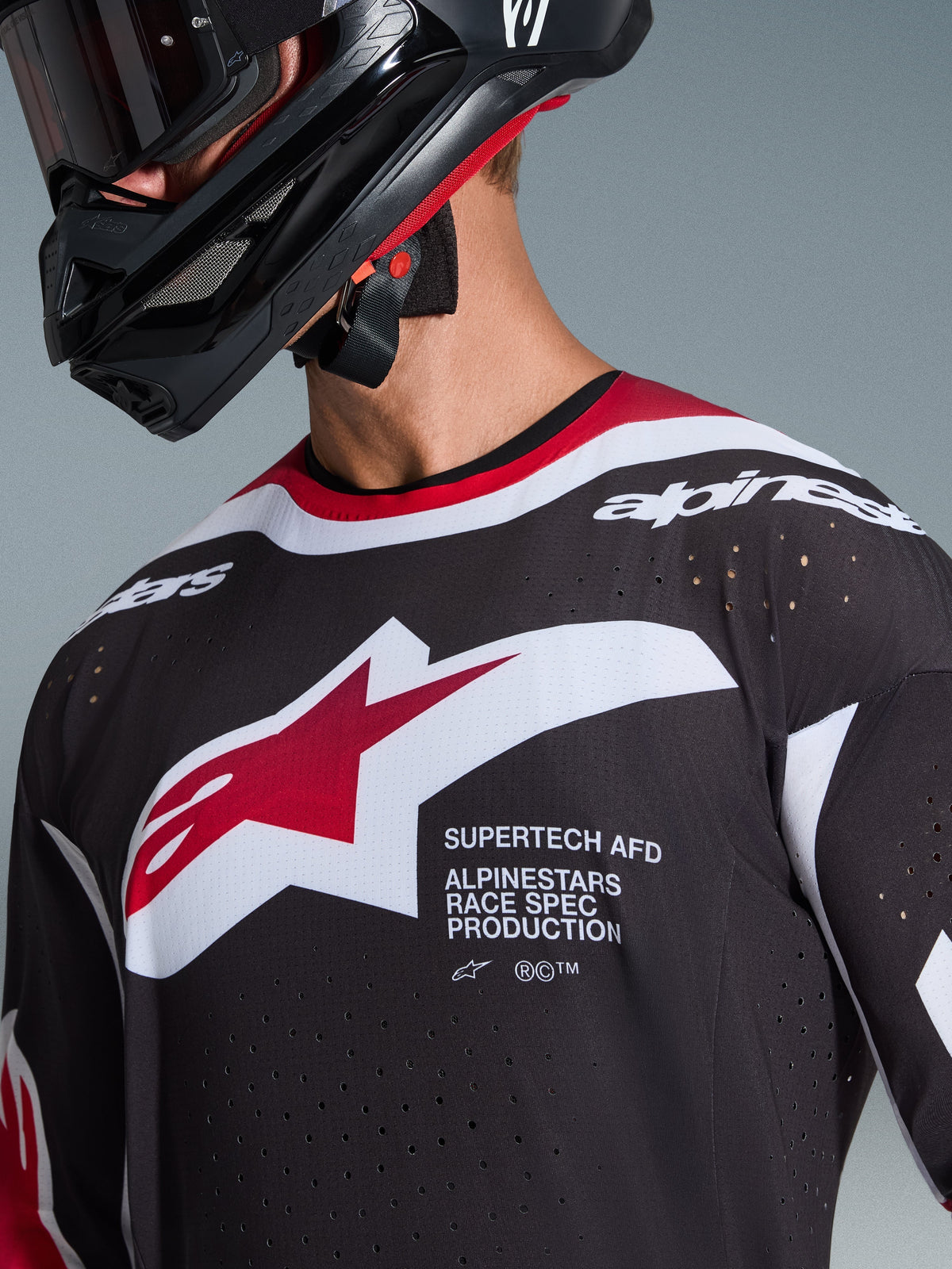 Alpinestars 2026 Supertech AFD Vista-tröja, svart, röd och vit, närbild på bröstet som visar Alpinestars stjärnlogotyp och 'Supertech AFD'-text, med laserskurna ventilationshål och meshkonstruktion, bärs med en svart motocrosshjälm.