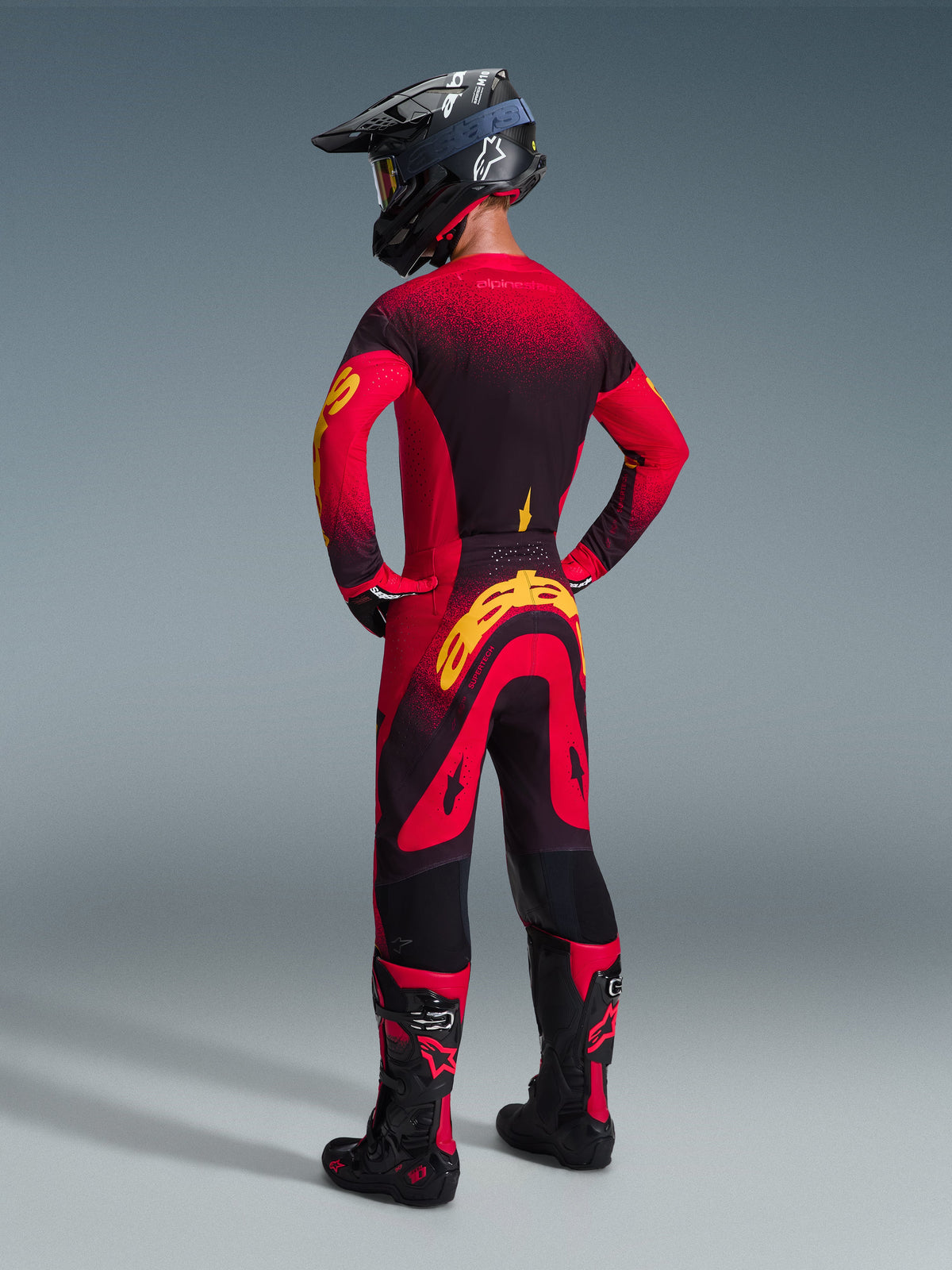 Motocross rider wearing the Alpinestars 2026 Supertech Scenz Gear Set, red and black jersey with yellow accents, matching pants with bold yellow logo on the back, black helmet and red-accented boots, coordinated outfit for professional motocross racing