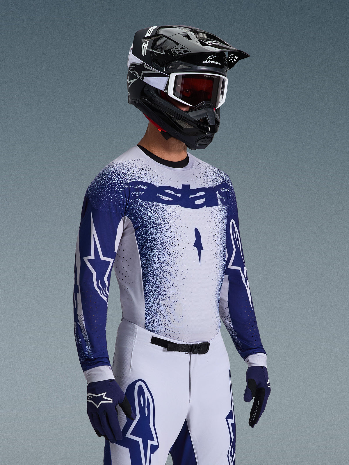 Motocrossförare i 2026 Supertech Scenz-tröja i ljusgrått och mörkblått, kombinerad med matchande vita och blå racingbyxor, blå handskar och en svart hjälm med vita goggles. Tröjan har en punktmönstrad blå gradienteffekt på bröstet och ärmarna, professionell atletisk passform och tydlig 'astars'-branding.