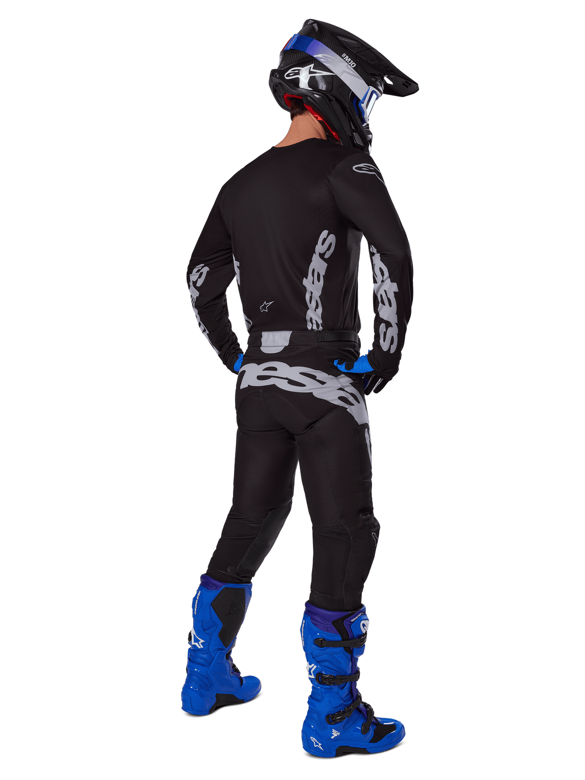 Motocrossförare sedd bakifrån i Alpinestars 2025 Racer Graphite Gear Set, svart och grå tröja och byxor med grå logotyper, kombinerat med klarblå motocross-stövlar, svart och blå hjälm samt blå handskar, komplett outfit för terrängkörning.
