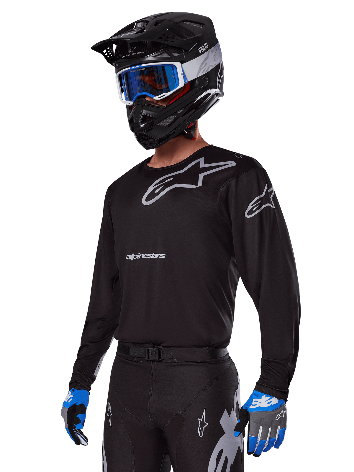 Motocrossförare i Alpinestars 2025 Racer Graphite-utrustningsset, svart tröja med grå Alpinestars-logotyper, matchande svarta byxor med grå detaljer, svart hjälm med blå och vita goggles, blå och grå handskar, teknisk outfit för terrängkörning