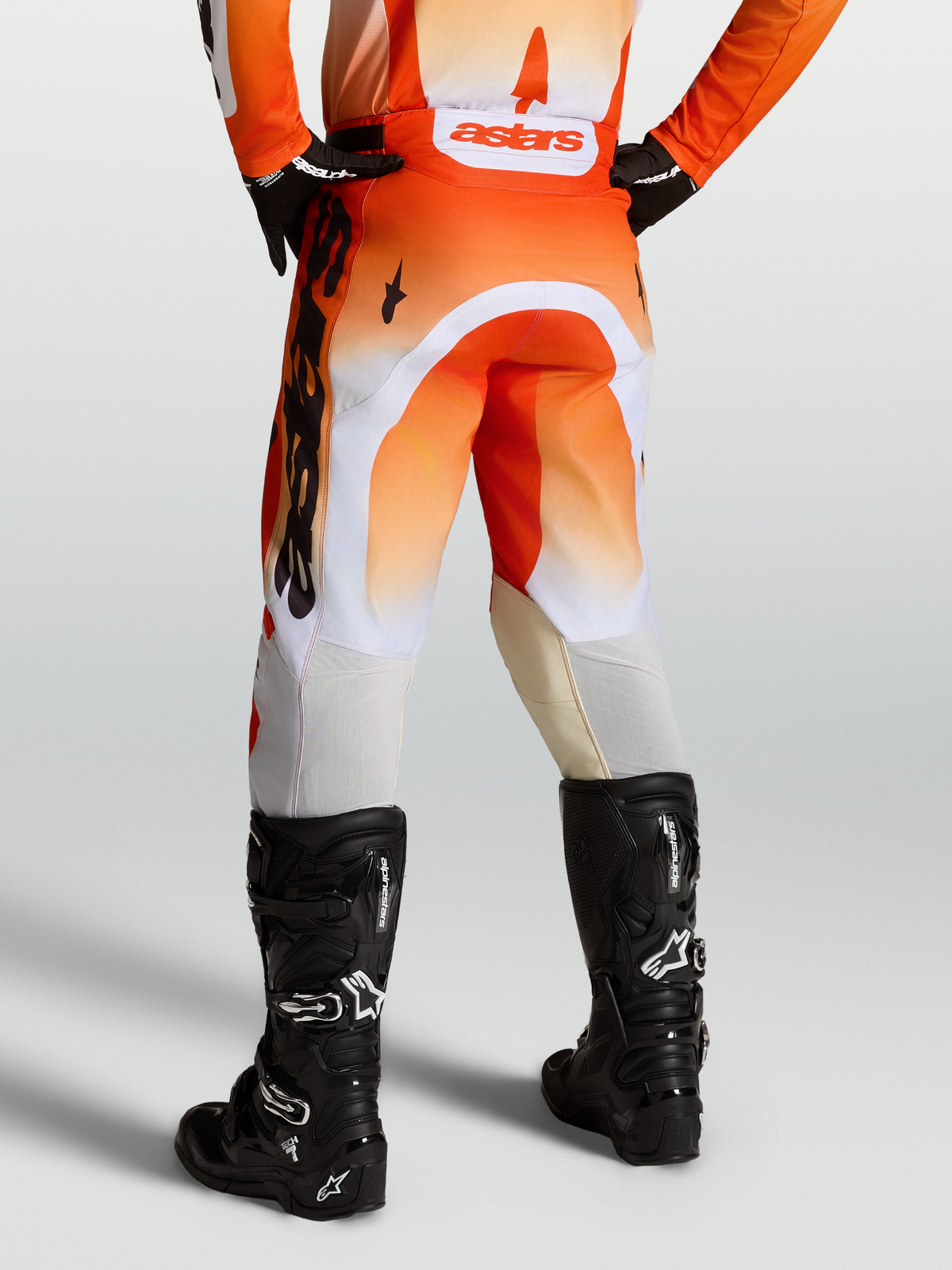 Alpinestars Racer Amber byxor, röda och orange motocrossbyxor för herr, hållbart 600D-material med vita stretchpaneler och svarta motorcykelstövlar, vy bakifrån
