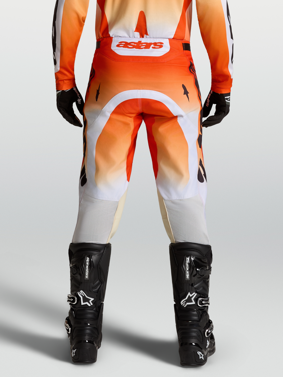 Alpinestars Racer Amber byxor, röda och vita motocrossbyxor sedda bakifrån på modell med svarta stövlar.