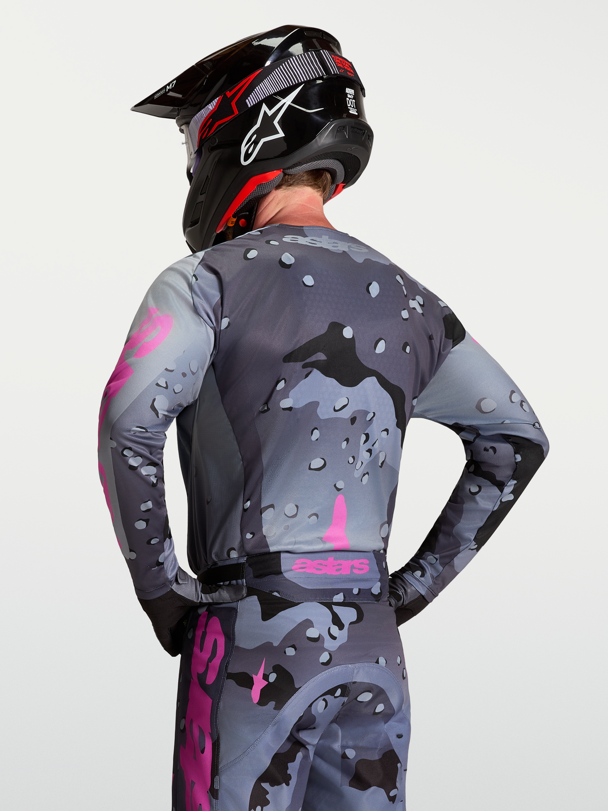 Alpinestars Racer Lone tröja bakifrån, grå och lila fuktransporterande motocrosströja i polytyg med kamouflagemönster, på modell med matchande byxor och hjälm.