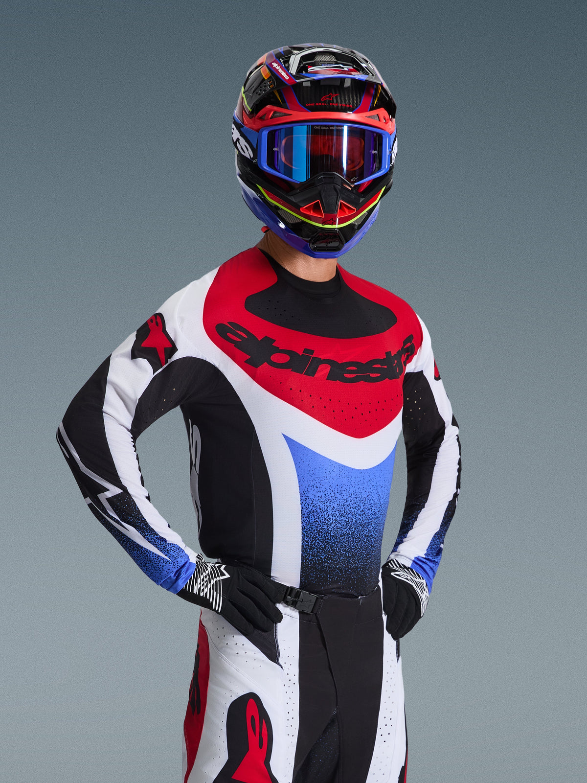 Alpinestars 2026 Techstar Knif Gear Set, Motocross rider in a red white and blue racing jersey with black accents, matching multi-color helmet and goggles, black gloves, professional gear for motocross competition.