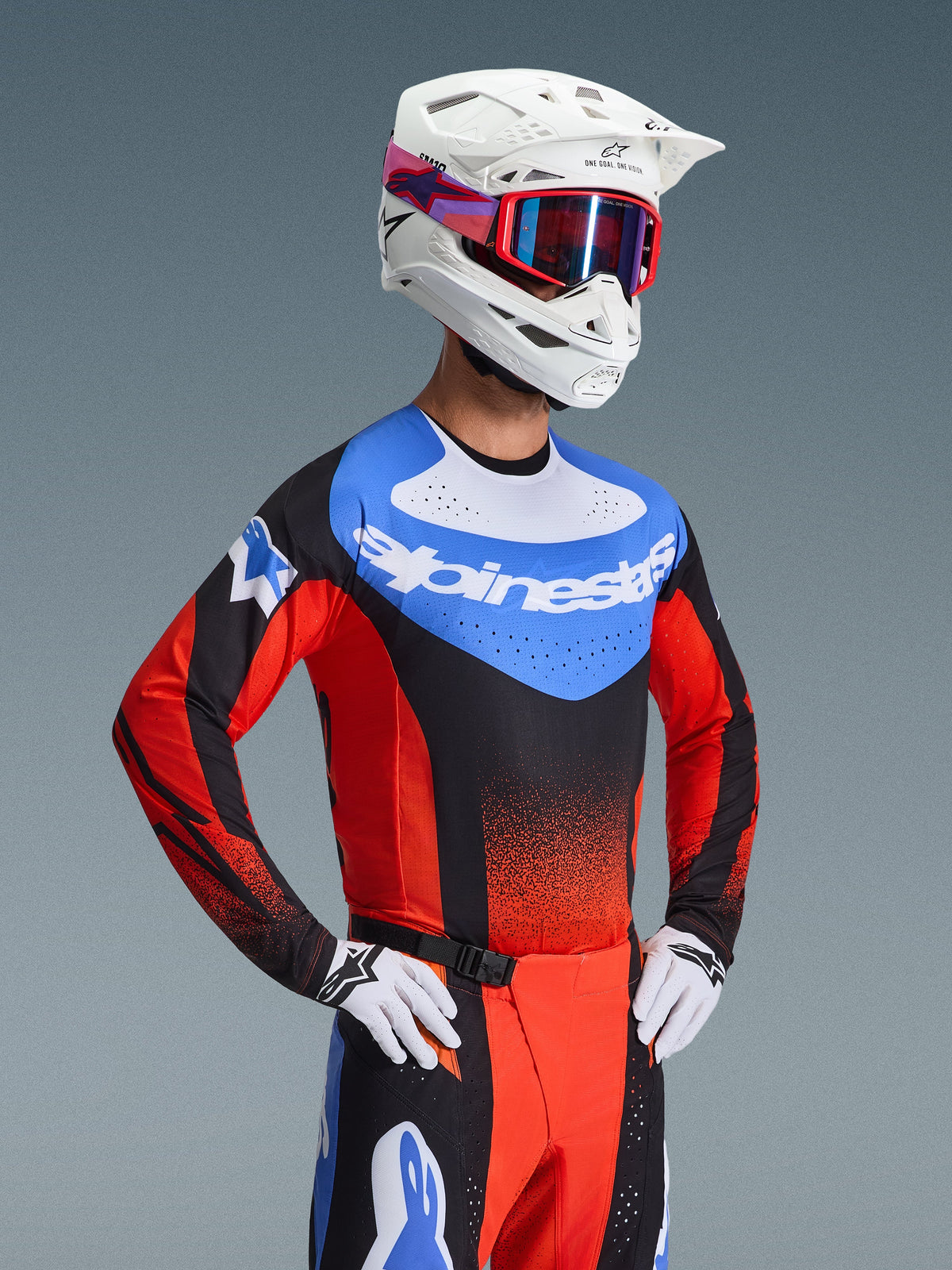 Motocross rider wearing Alpinestars 2026 Techstar Knif Gear Set, blue jersey with white branding and red sleeves, matching black and red pants with blue accents, white helmet with red goggles, white and black gloves, professional racing outfit for motocross