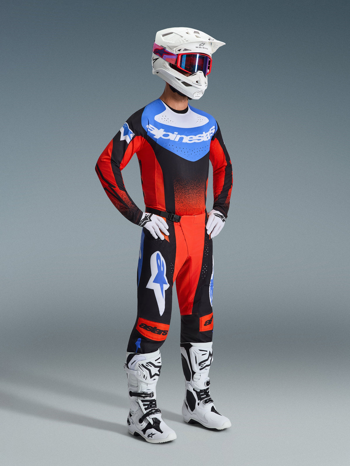 Motocross rider wearing the Alpinestars 2026 Techstar Knif Gear Set, Jersey features a blue chest with white logo and red sleeves with black gradients, matching black and red pants with blue star accents, white helmet with red and blue goggles, white and black boots, and white gloves.