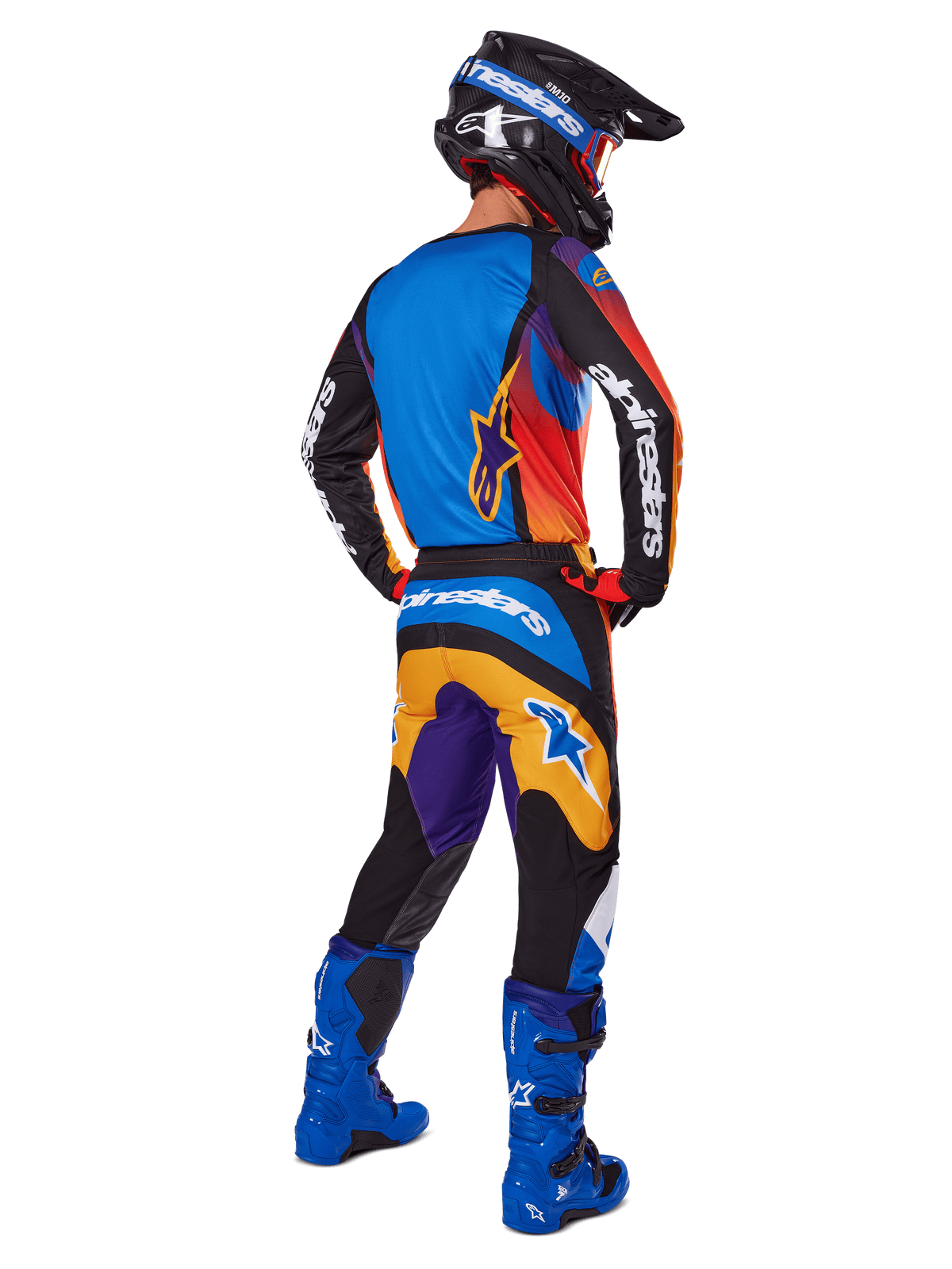 Motocrossförare sedd bakifrån iklädd Alpinestars 2025 Fluid Wurx-utrustningsset, flerfärgad tröja med blå, orangea och lila paneler, matchande byxor med vit Alpinestars-logotyp på sätet, klarblå stövlar och svart hjälm, koordinerad outfit för terrängkörning
