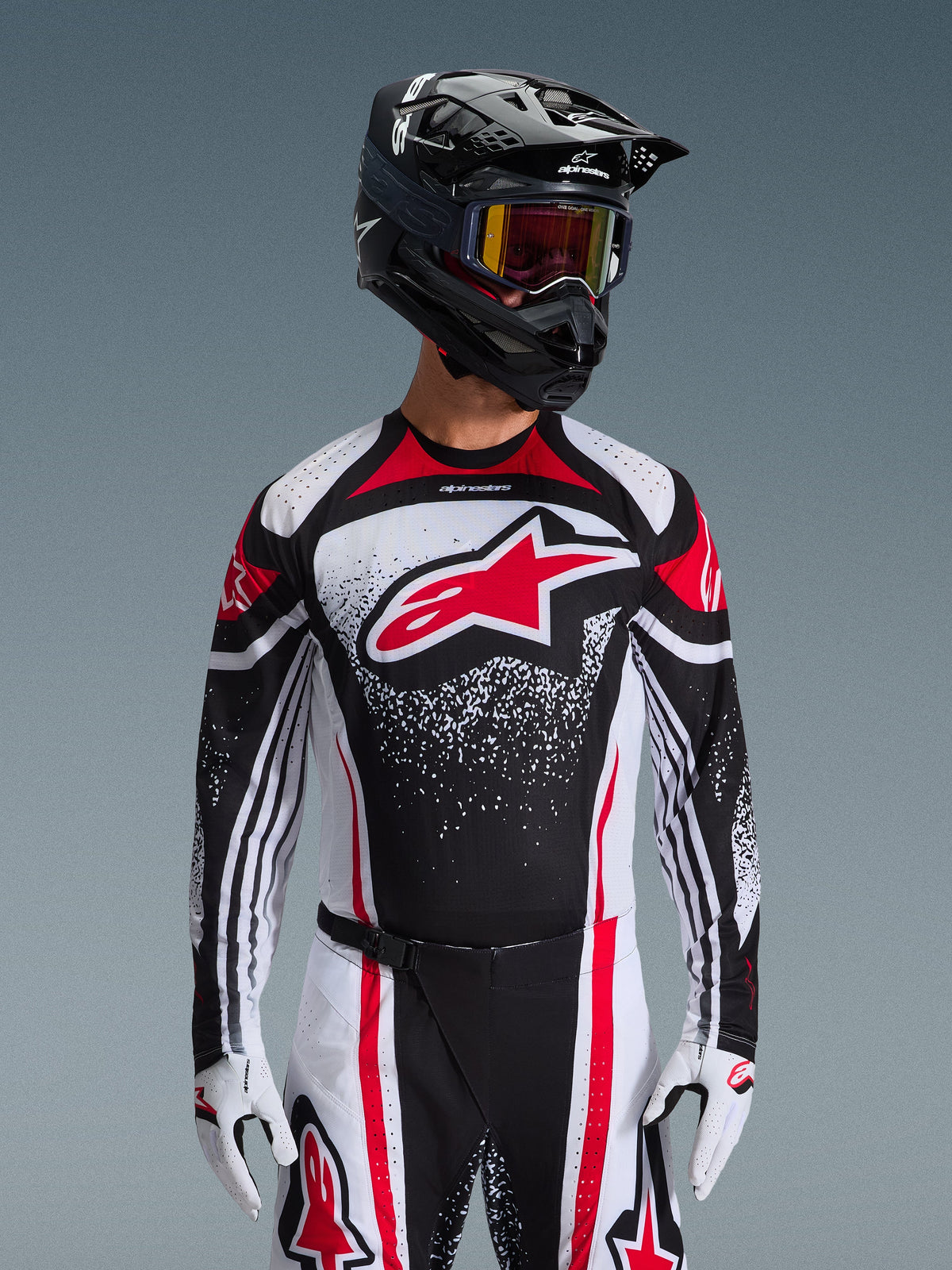 Alpinestars 2026 Techstar Nomur-utrustningsset, motocrosströja och byxor, svart, vit och röd, med en stor röd logotyp på bröstet och en spräcklig grafisk design, bärs med en svart hjälm, röda goggles och vita handskar, professionell atletisk racingpassform för terrängkörning.