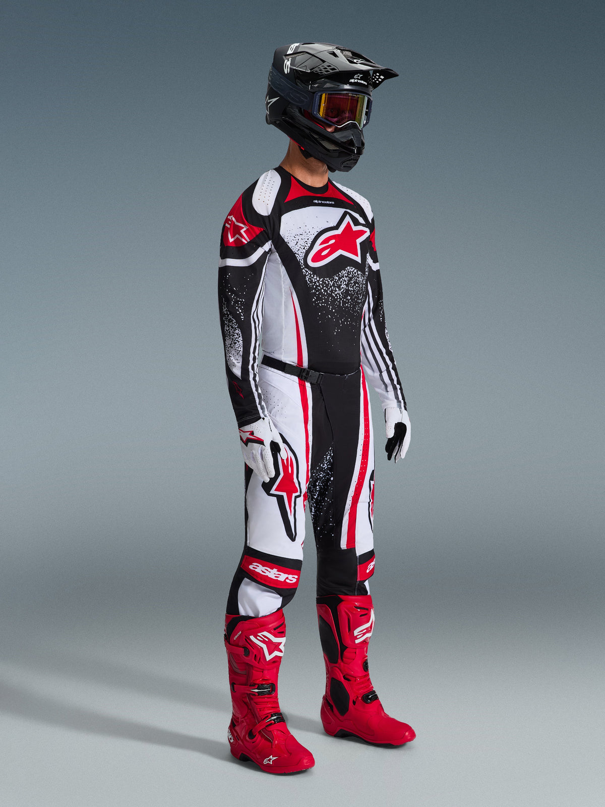 Motocrossförare iklädd Alpinestars 2026 Techstar Nomur utrustningsset, svart tröja med röda och vita grafiska mönster, matchande motocrossbyxor, klarröda stövlar, svart hjälm med goggles, koordinerad racingoutfit för terrängkörning