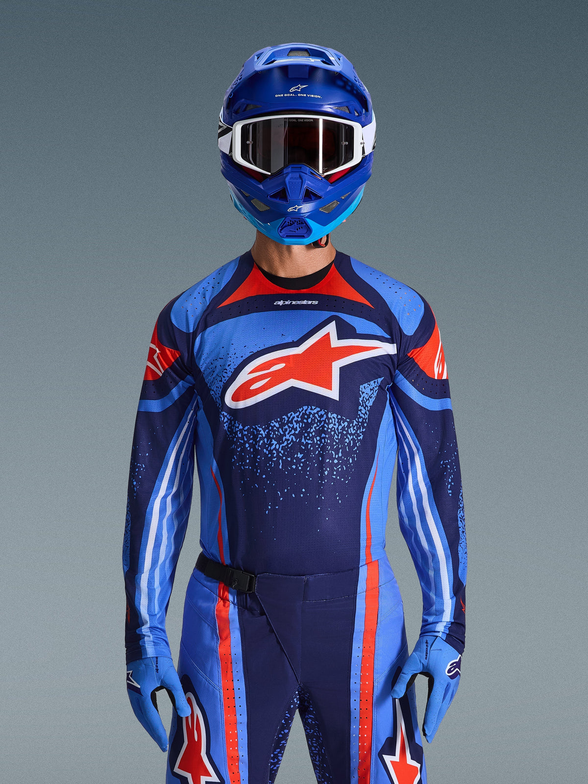 Alpinestars 2026 Techstar Nomur Jersey, Motocross Racing Jersey, Dark Navy, Orange, and UCLA Blue, worn with matching pants, blue helmet, and gloves, featuring a white star logo on the chest with dynamic lines and speckled patterns