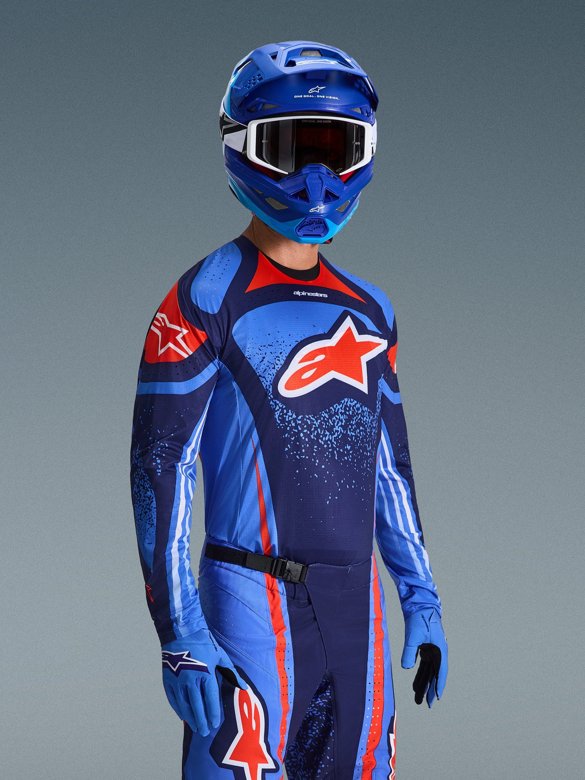 Motocrossförare i Alpinestars 2026 Techstar Nomur-tröja, racingutrustning i färgerna Dark Navy, orange och UCLA Blue, med en stor orange Astars-logotyp, matchande blå hjälm och handskar, atletisk tävlingsoutfit för terrängkörning.