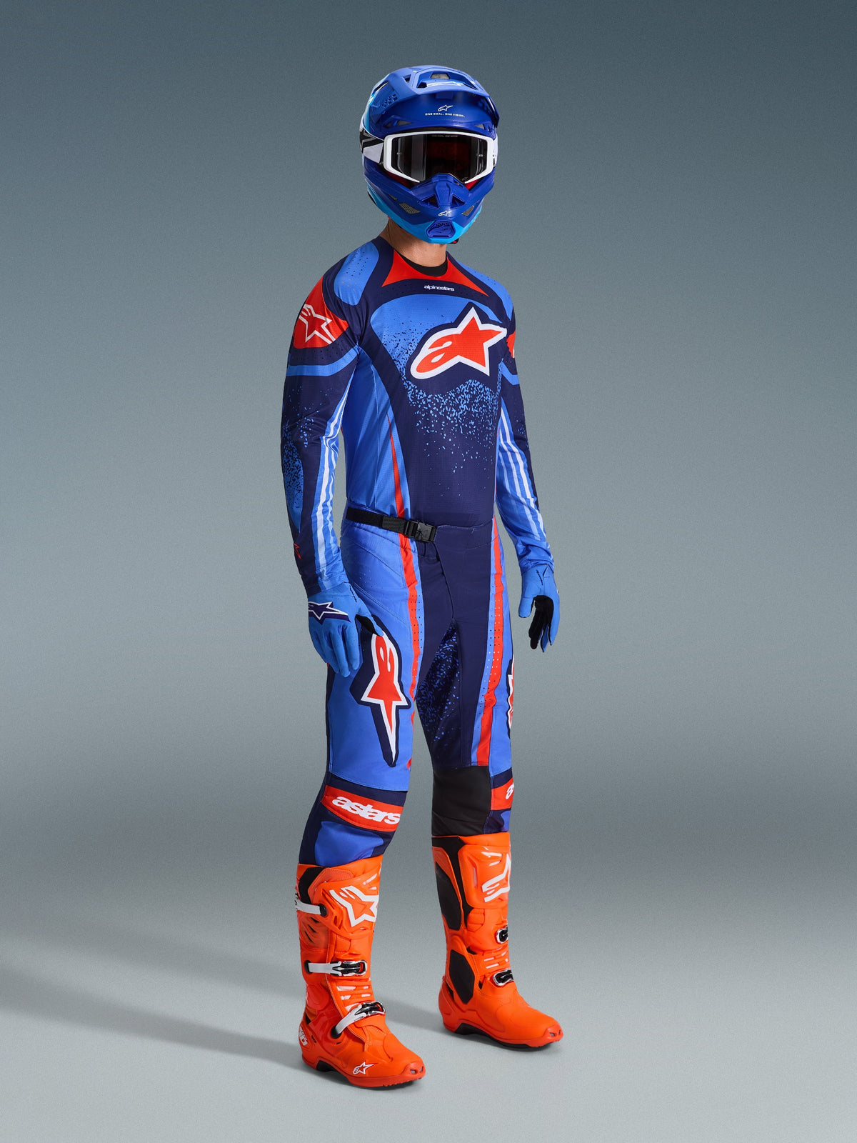 Motocrossförare i komplett racingutrustning, blå och mörkblå Techstar Nomur-tröja med orange Alpinestars-logotyp, matchande blå och mörkblå byxor med orange detaljer, blå hjälm med vita goggles, klara orange stövlar och blå handskar, koordinerad outfit för terrängkörning