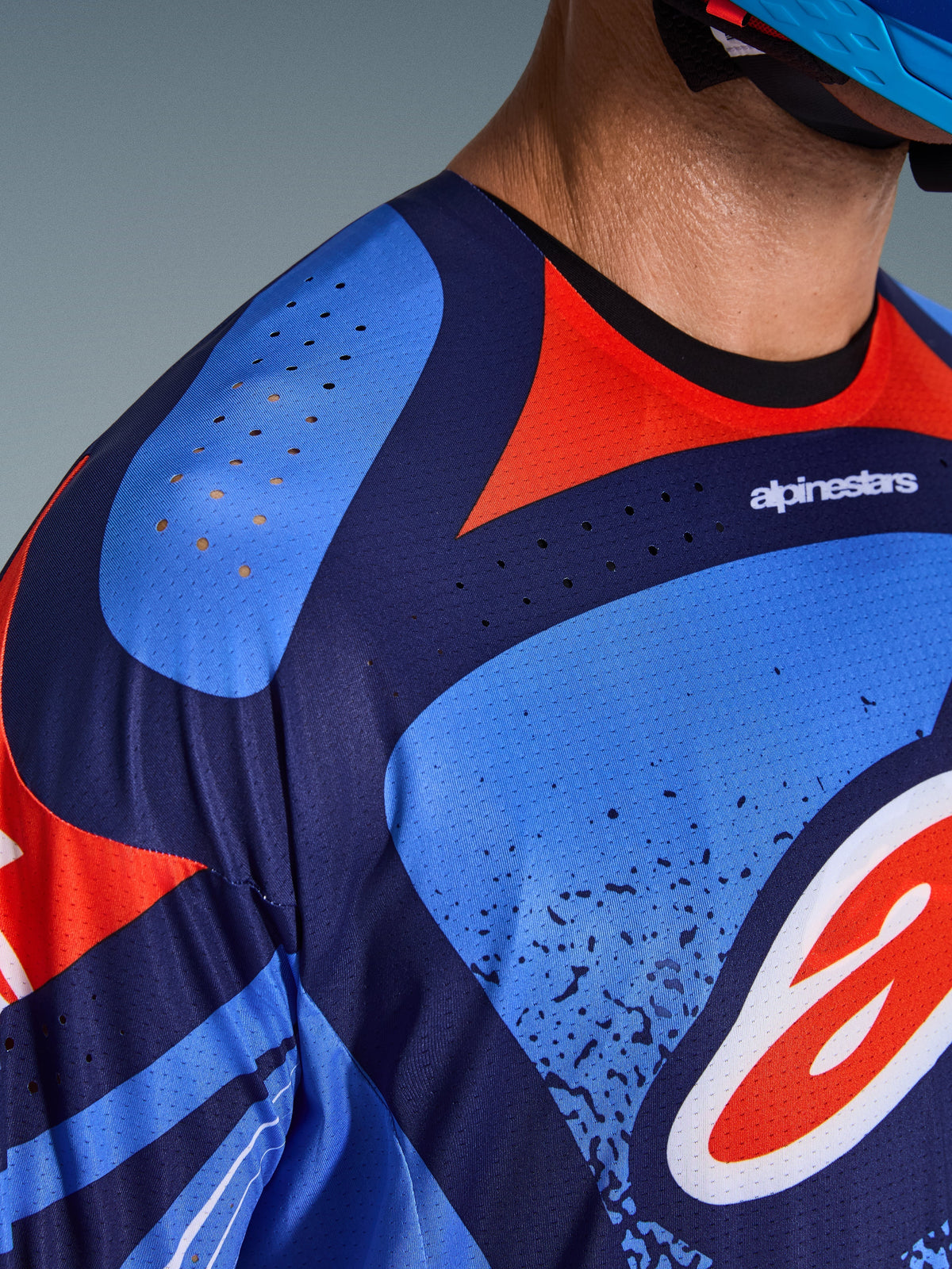 Närbild på Alpinestars 2026 Techstar Nomur-tröja, motocrosströja i mörkblått, orange och UCLA-blått, med laserskurna ventilationshål på axel och bröst, tekniskt fukttransporterande material och atletisk tävlingspassform
