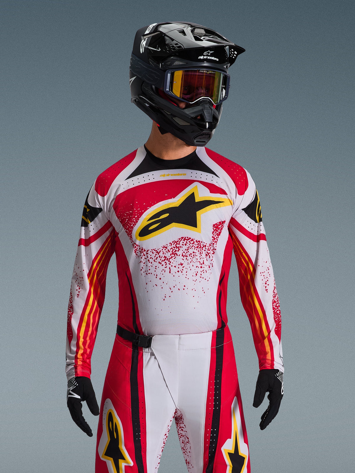 Alpinestars 2026 Techstar Nomur-tröja, motocrosströja, röd, vit och svart, med en stor svart A-star-logotyp på bröstet med gula detaljer, röd splatter-design, bärs med en svart hjälm och matchande off-road-utrustning