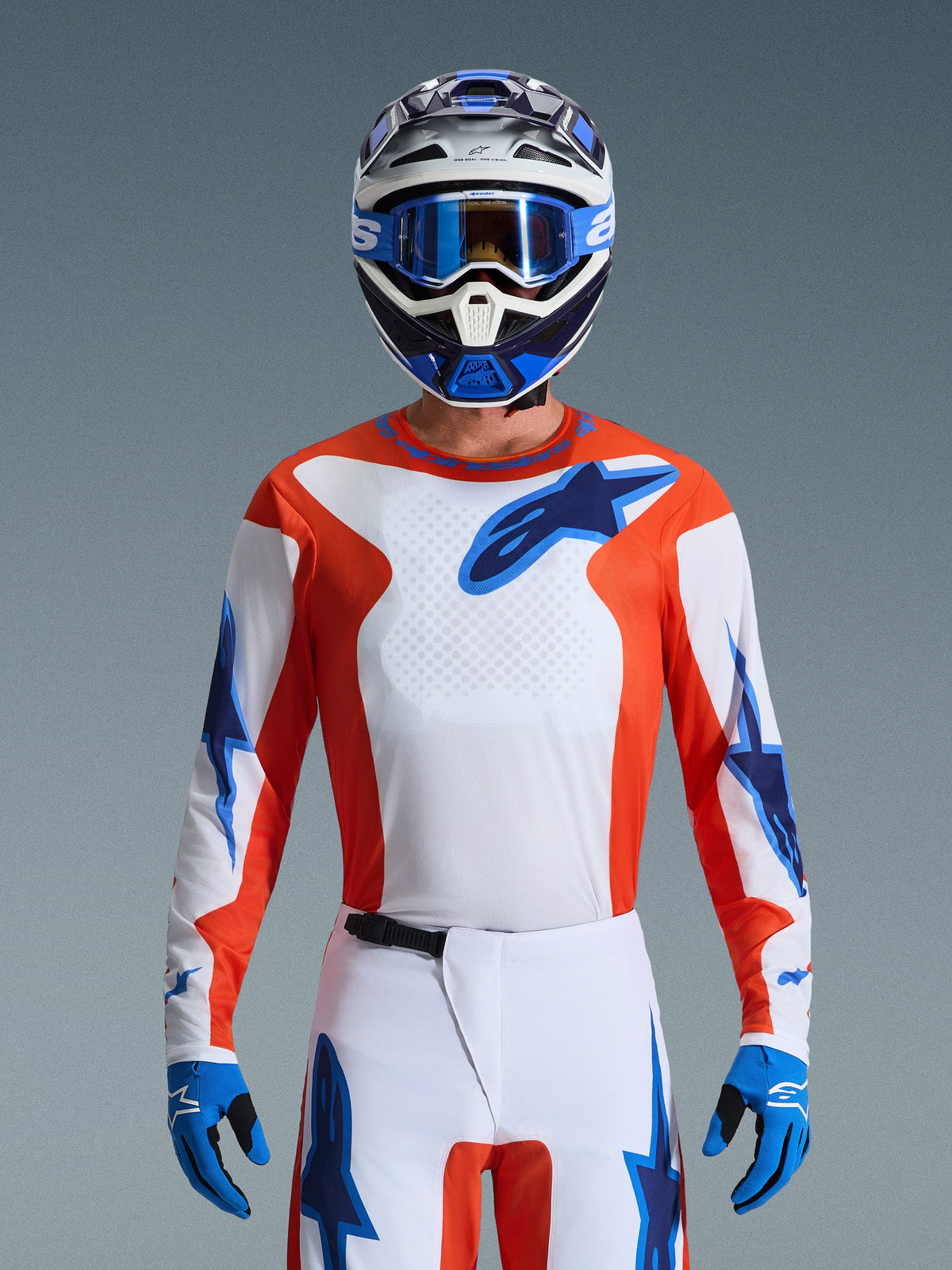 Alpinestars 2026 Fluid Grid utrustningsset, motocrossförare i orange och vit tröja med blå stjärnlogotyper, vita byxor med blå detaljer, matchande blå och vit hjälm med blå goggles och handskar, komplett outfit för terrängkörning