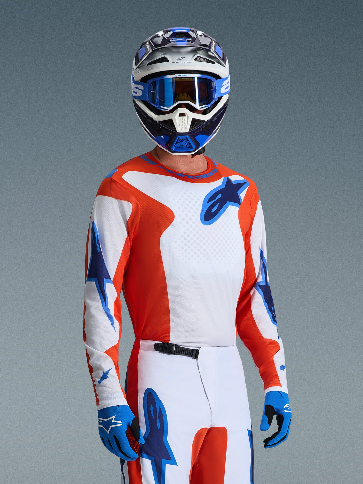Motocrossförare som bär Alpinestars 2026 Fluid Grid-utrustningsset, orange och vit tröja med blå stjärnlogotyper, vita och orangea byxor med blå detaljer, blå handskar, blå och vit hjälm med blå goggles, koordinerad atletisk racingutrustning för terrängkörning