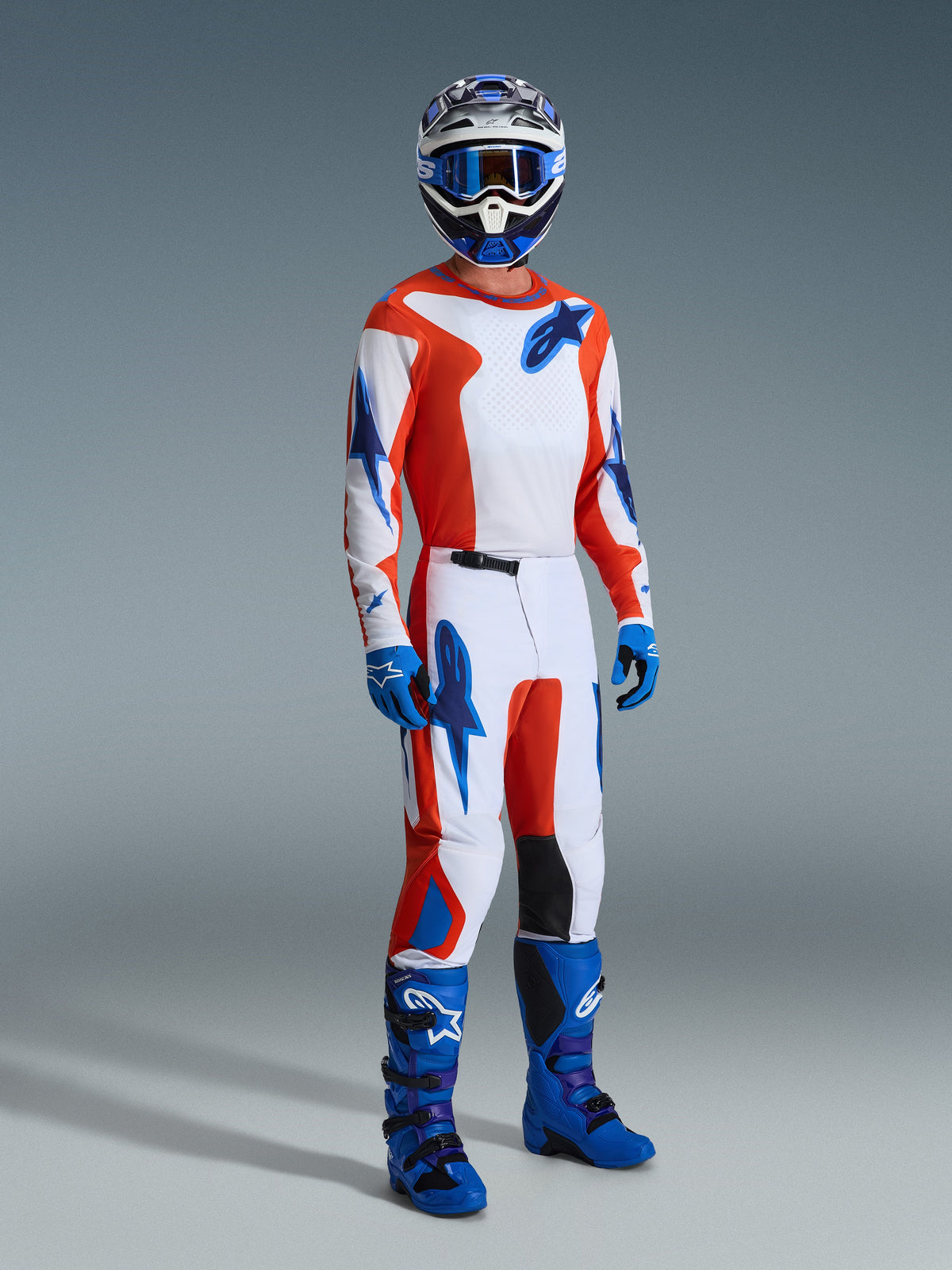 Motocrossförare i Alpinestars 2026 Fluid Grid-utrustningsset, vit tröja och byxor med orange och UCLA-blå grafik, matchande blå hjälm och goggles, blå handskar och klarblå racingstövlar, koordinerad outfit för terrängkörning.