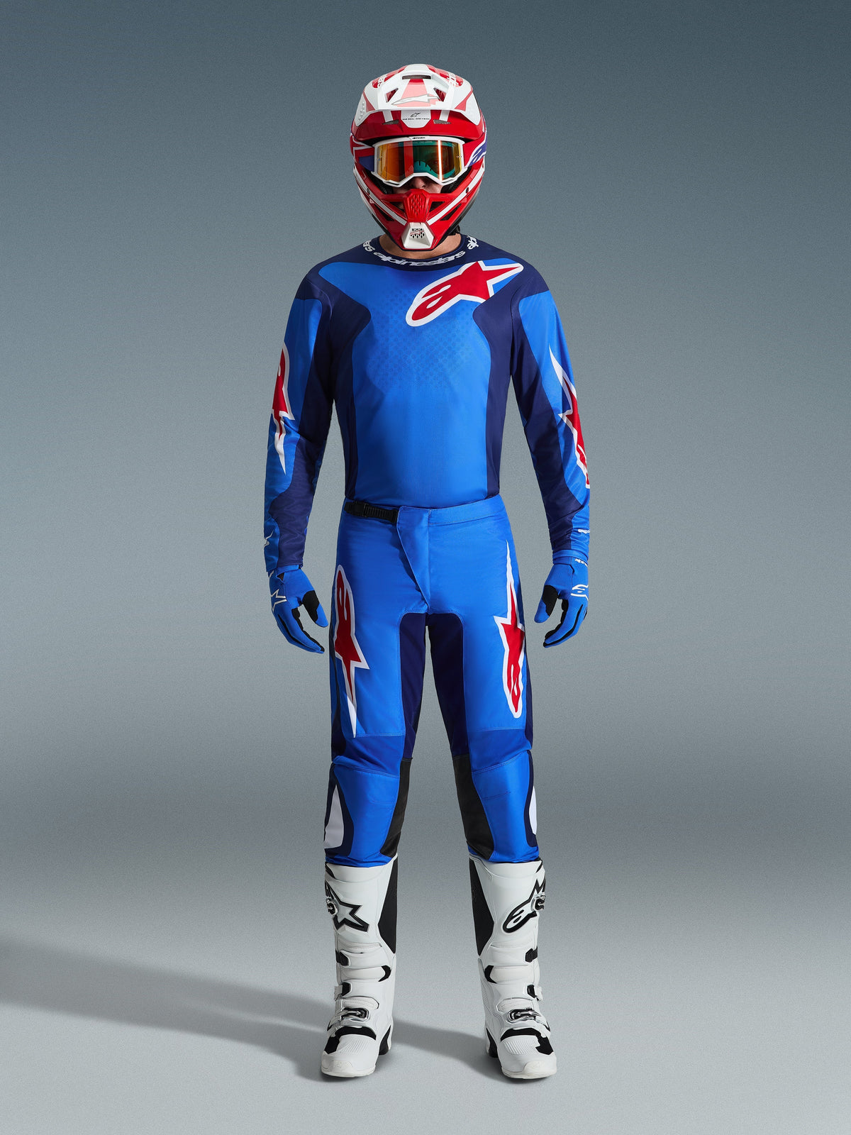 Motocrossförare iklädd Alpinestars 2026 Fluid Grid-tröja i blått och rött, matchande blå byxor med vita och röda stjärnlogotyper, röd och vit hjälm med spegelglasgoggles, blå handskar och vita och svarta racingstövlar, komplett off-road-utrustning.