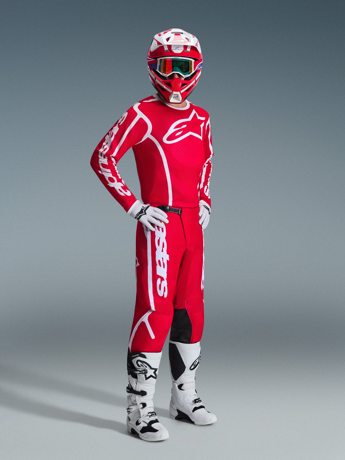Motocrossförare i komplett Alpinestars racingutrustning, med 2026 Fluid Apex-tröja i rött och vitt, matchande röda byxor med vit logotyp, röd och vit hjälm med goggles, vita och svarta motocross-stövlar och vita handskar, professionell studiobild av terrängutrustning.