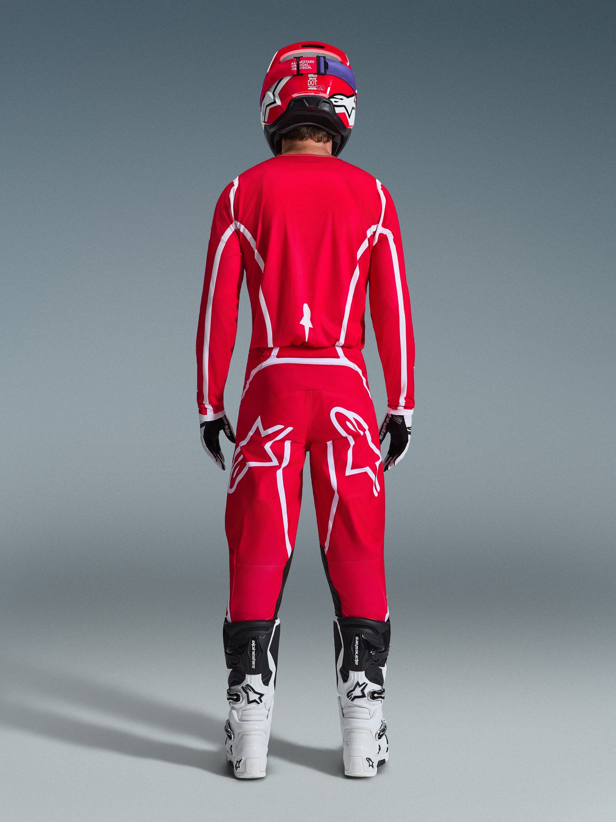 Motocrossförare sedd bakifrån i Alpinestars 2026 Fluid Apex-tröja i rött och vitt, matchande röda byxor med framträdande vita stjärnlogotyper, röd hjälm, vita och svarta motocross-stövlar och svarta och vita handskar, komplett kit för terrängkörning