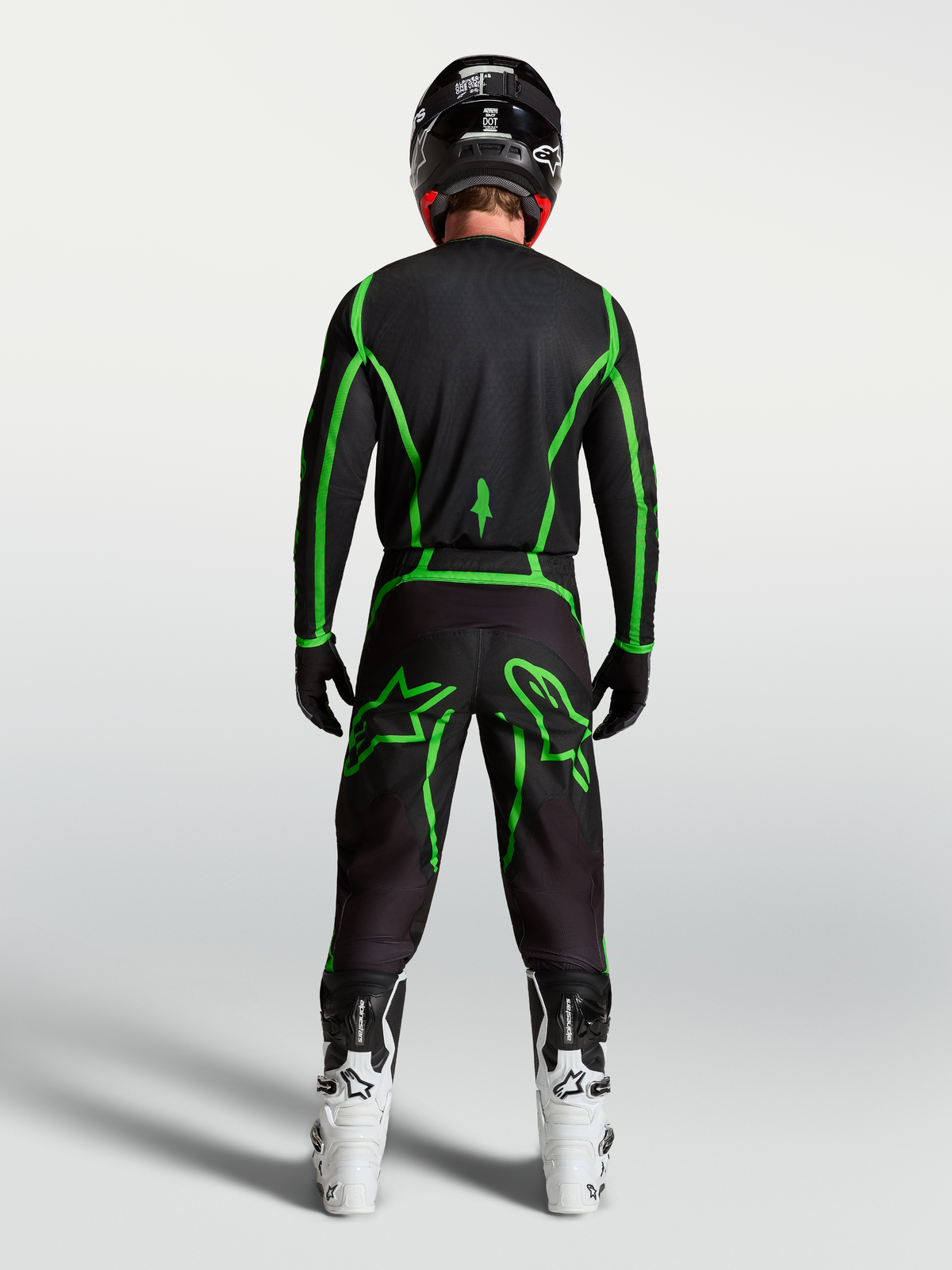 Alpinestars Fluid Apex V2 tröja, motocrossutrustning, svart och neongrön, vy bakifrån på förare med vita MC-stövlar.