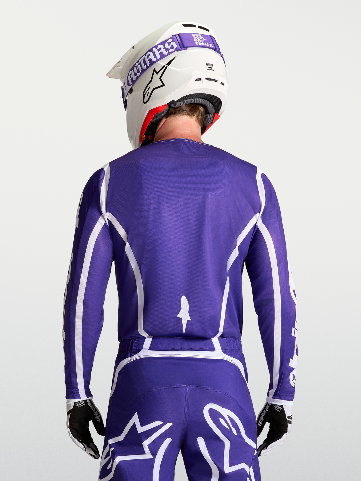 Alpinestars Fluid Apex V2 tröja, motocrosströja i mörkblått och vitt, vy bakifrån på modell med matchande byxor och hjälm för terrängkörning.