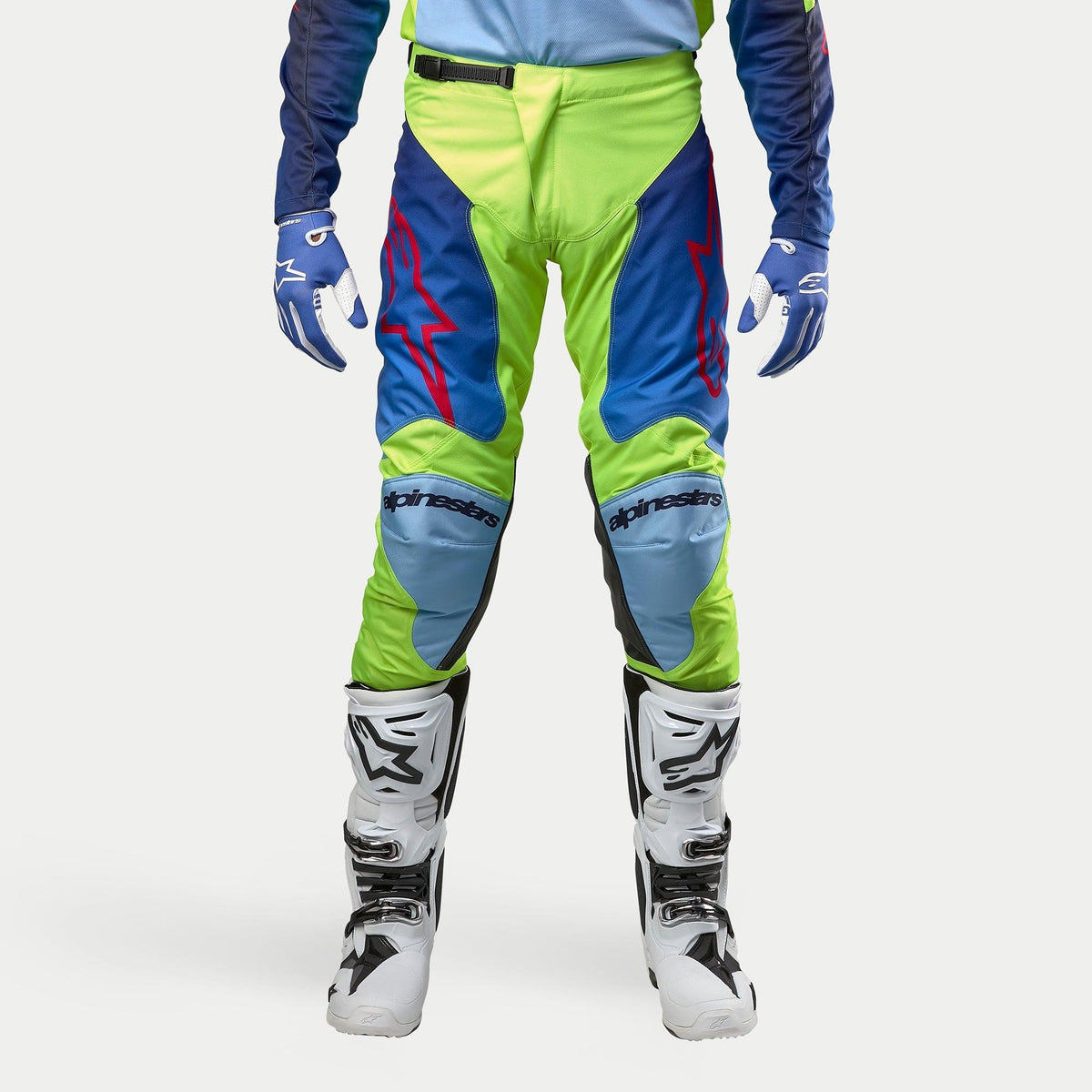 Alpinestars 2024 Racer Hoen byxor, motocrossbyxor, gul fluo och mörkblå, bärs med vita och svarta motocross-stövlar och blå handskar, med framträdande röda logotyper, ljusblå knäpaneler och en sportig ergonomisk design för terrängkörning
