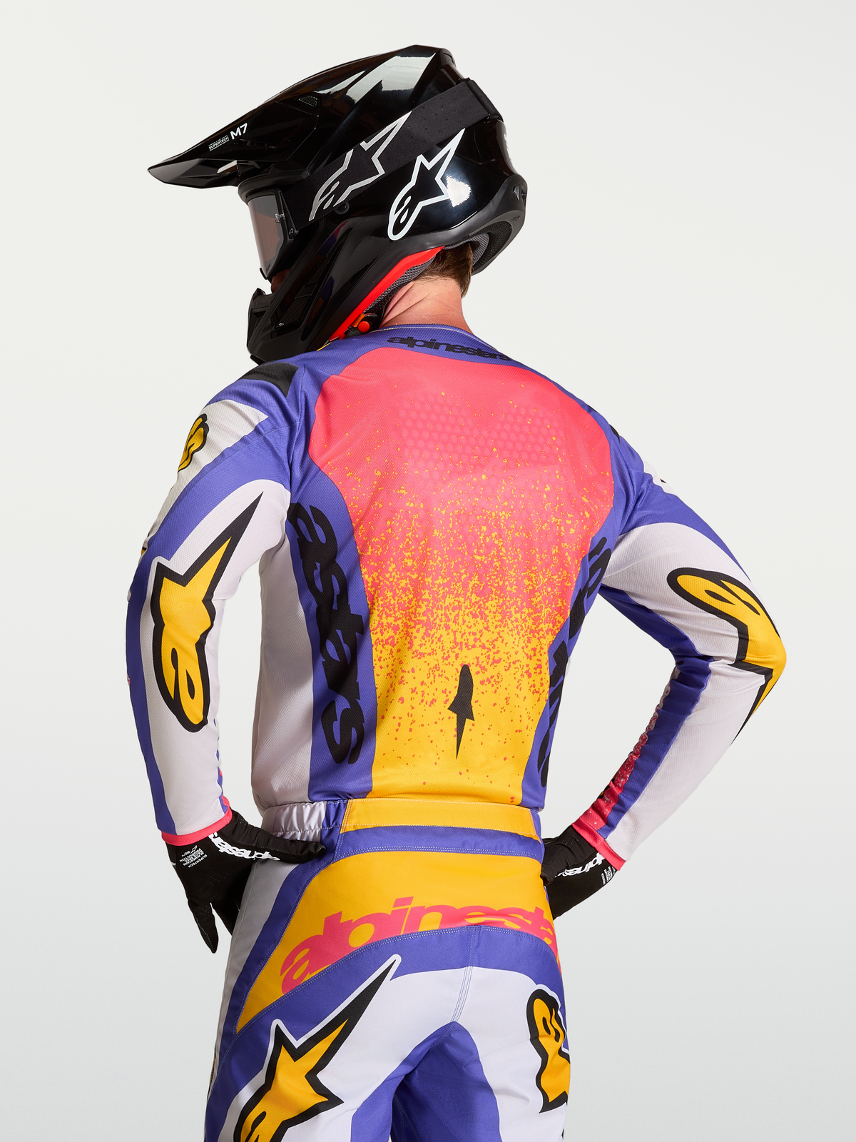 Alpinestars Fluid Drag Jersey, Blue Iris and Gold motocross riding jersey on a model wearing an Alpinestars helmet, featuring moister-wicking fabric and an ergonomic rear cut.