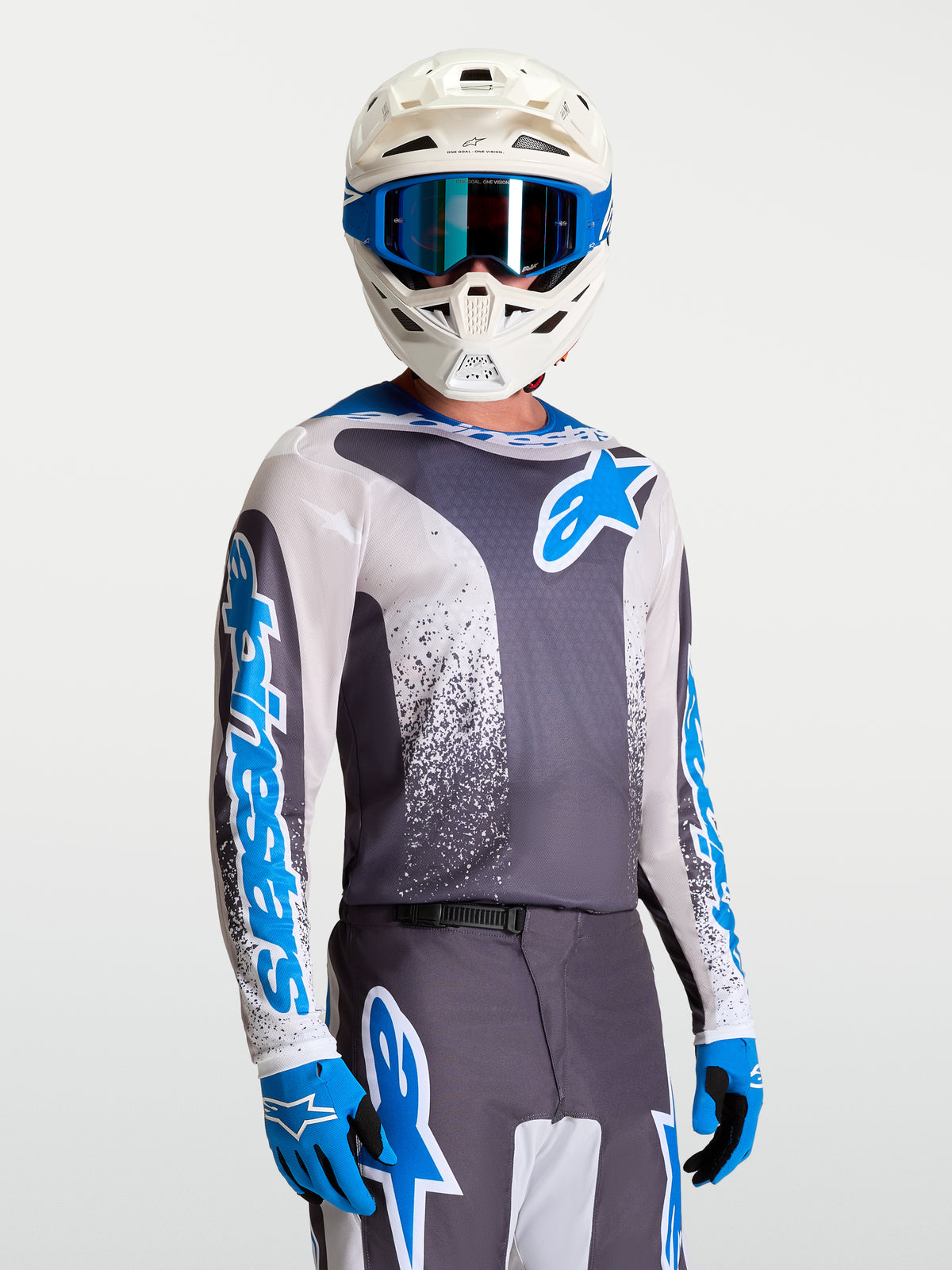 Alpinestars Fluid Drag tröja, grå och blå motocrosströja för terrängkörning, bärs av modell med vit hjälm och blå handskar.