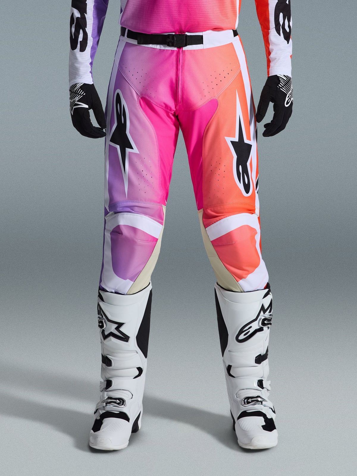 Alpinestars 2026 Racer Air Portl-byxor, motocrossbyxor, livfull gradient i lila, rosa och orange, framträdande stjärnlogotyper på låren, bärs med vita racingstövlar och svarta handskar, designade för högpresterande terrängkörning