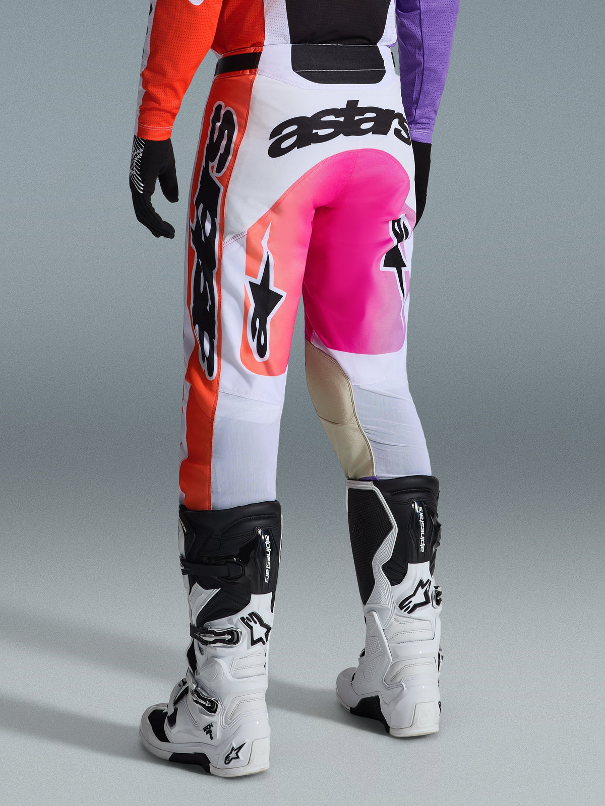 Alpinestars 2026 Racer Air Portl byxor, motocrossbyxor, flerfärgade med vitt, starkt rosa och orange, vy bakifrån bärs med vita och svarta Alpinestars-stövlar, med framträdande logotyper och slitstark racingkonstruktion
