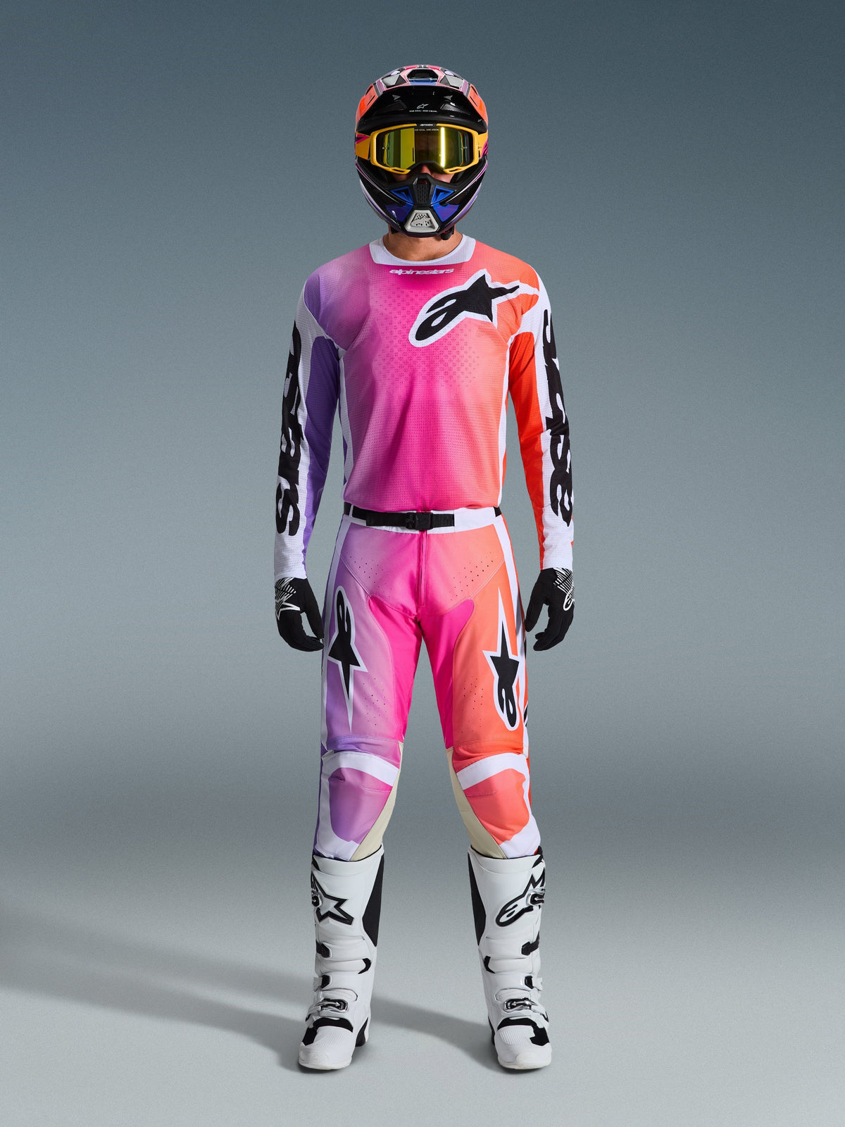 Motocrossförare i komplett Alpinestars 2026 Racer Air Portl-utrustning, med en rosa, lila och orange gradientdesign på byxor och tröja, matchande hjälm, gula goggles, vita stövlar och svarta handskar för en koordinerad terränglook.