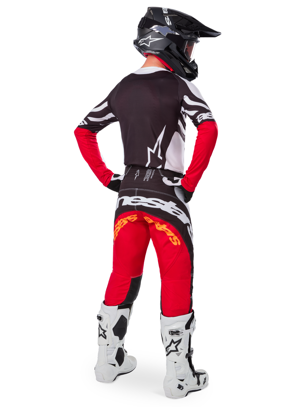 Motocrossförare sedd bakifrån i Limited Edition Techstar Deep-utrustningsset, med en svart tröja med vita och röda detaljer, matchande röda och svarta byxor med Alpinestars-logotyp, vita racingstövlar och en svart hjälm, som visar den kompletta utrustningen för terrängkörning.
