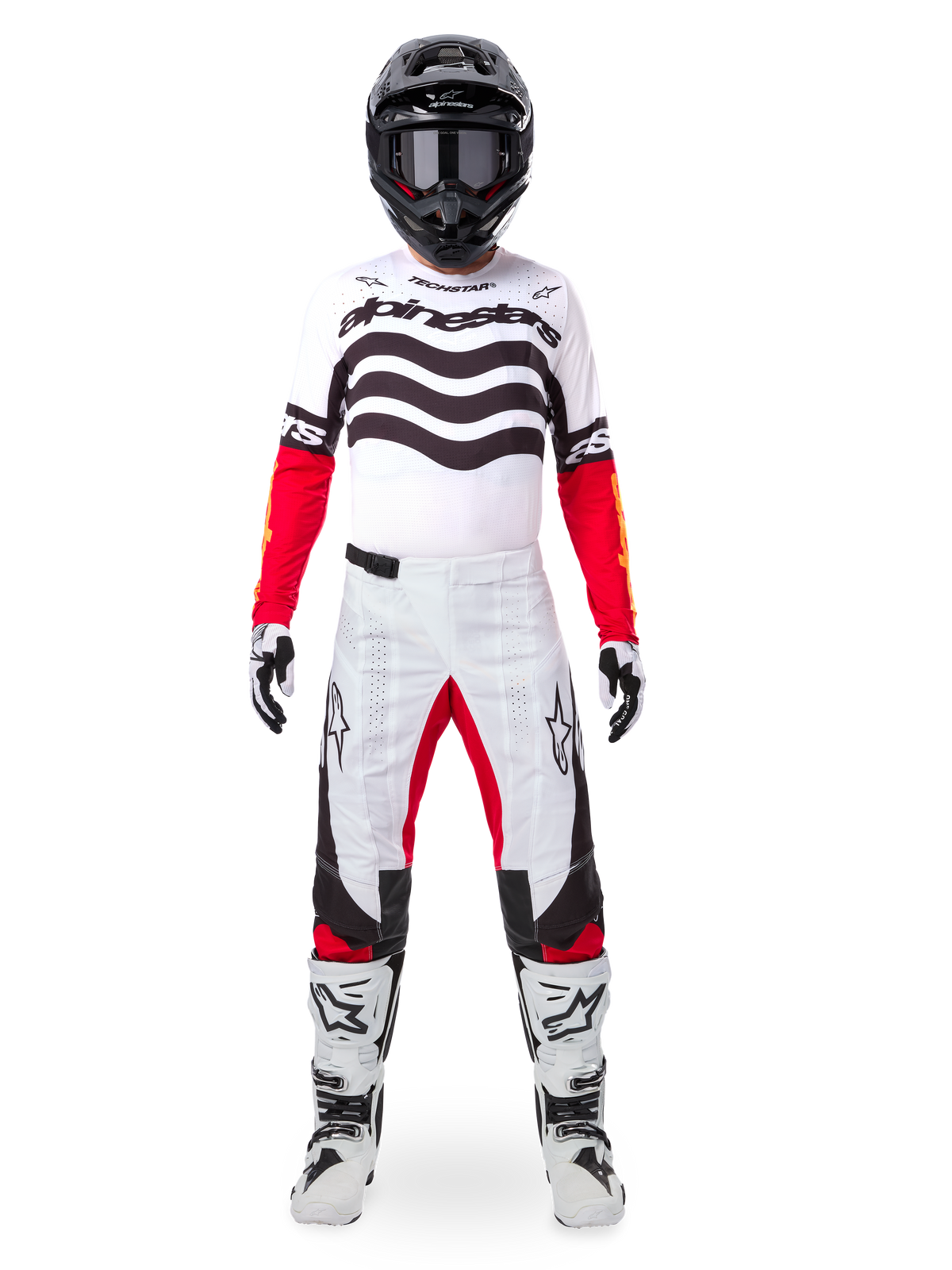 Motocrossförare klädd i Alpinestars Limited Edition Techstar Deep Gear Set, vit tröja med svart våggrafik och röda ärmar, matchande vita och svarta byxor med röda detaljer på insidan av låren, svart hjälm med mörka goggles och vita stövlar, komplett professionell outfit för terrängkörning