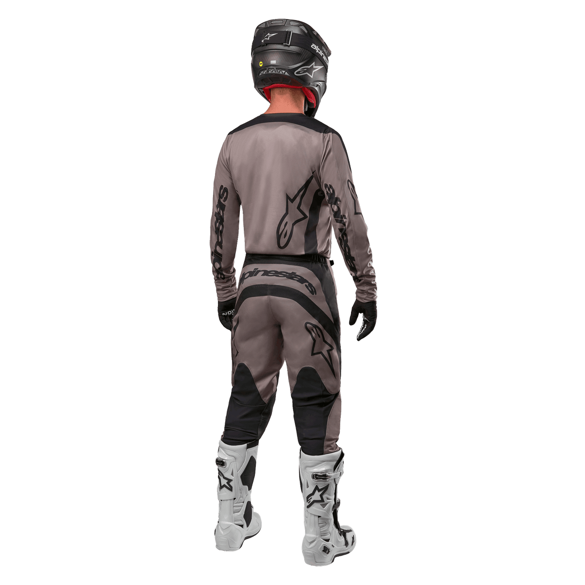 Alpinestars 2024 Fluid Lurv tröja, motocrosströja, Mud Black, bakifrån av en motocrossförare som bär matchande racingutrustning, svart hjälm och vita stövlar, med framträdande svarta Alpinestars-logotyper och en atletisk passform för terrängkörning.