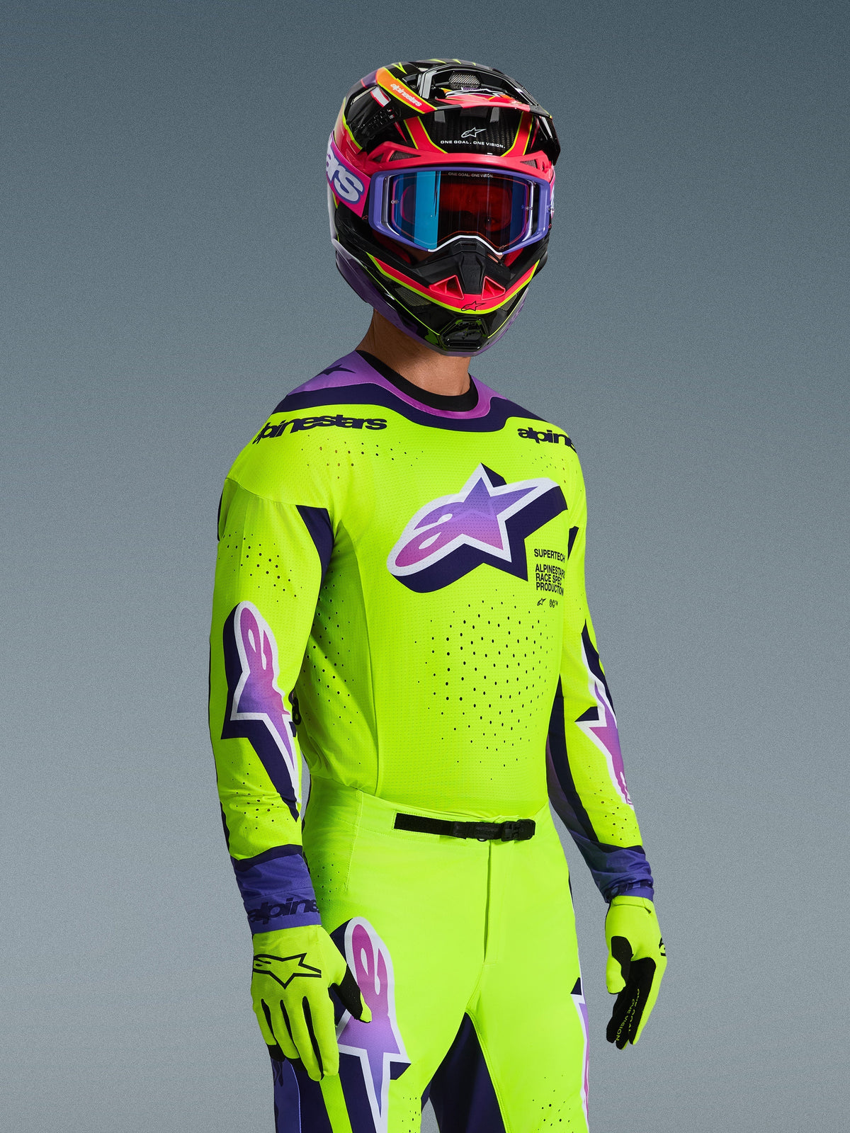 Motocrossförare i Alpinestars 2026 Supertech Vista-tröja och matchande utrustningsset, klar gul med lila och svarta detaljer, stor lila Astar-logotyp på bröstet och ärmarna, matchande handskar, flerfärgad racinghjälm med goggles, atletisk passform på proffsnivå för terrängkörning