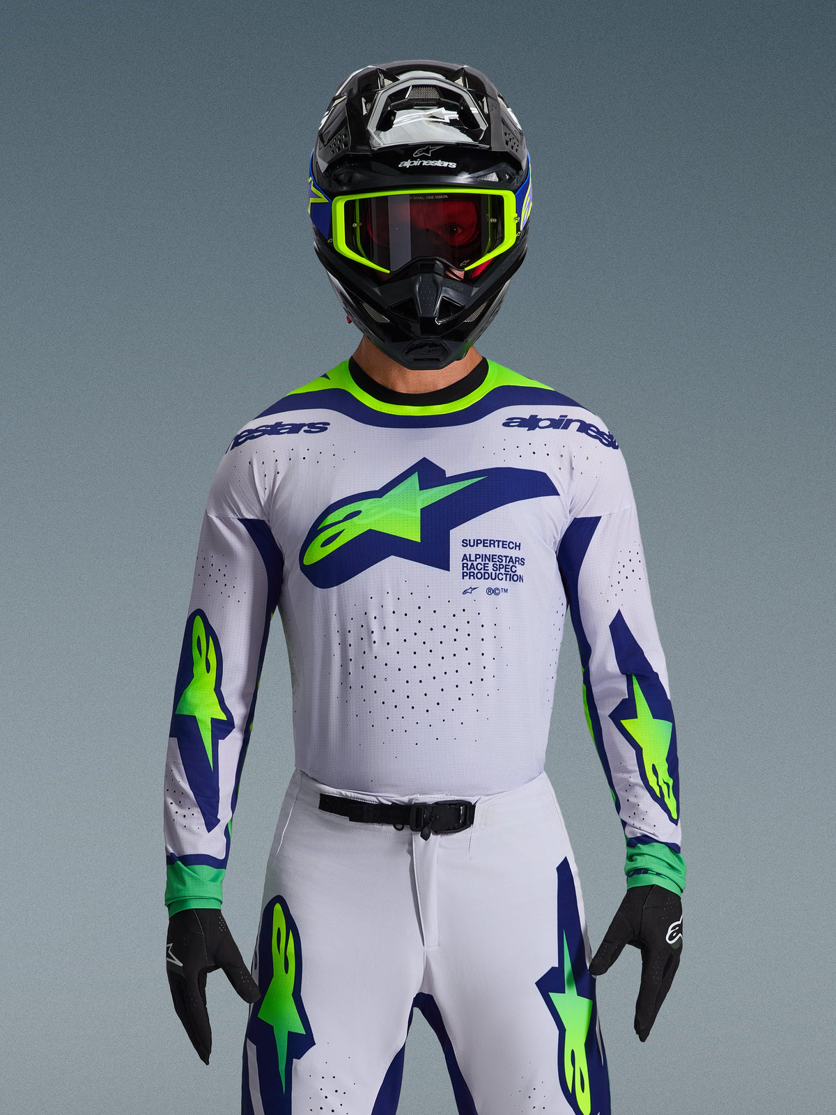 Alpinestars 2026 Supertech Vista Gear Set, Motocross Jersey and Pants, White with Blue and Neon Green graphics, worn with a black helmet and neon goggles, featuring laser-cut ventilation and athletic race fit for professional racing.