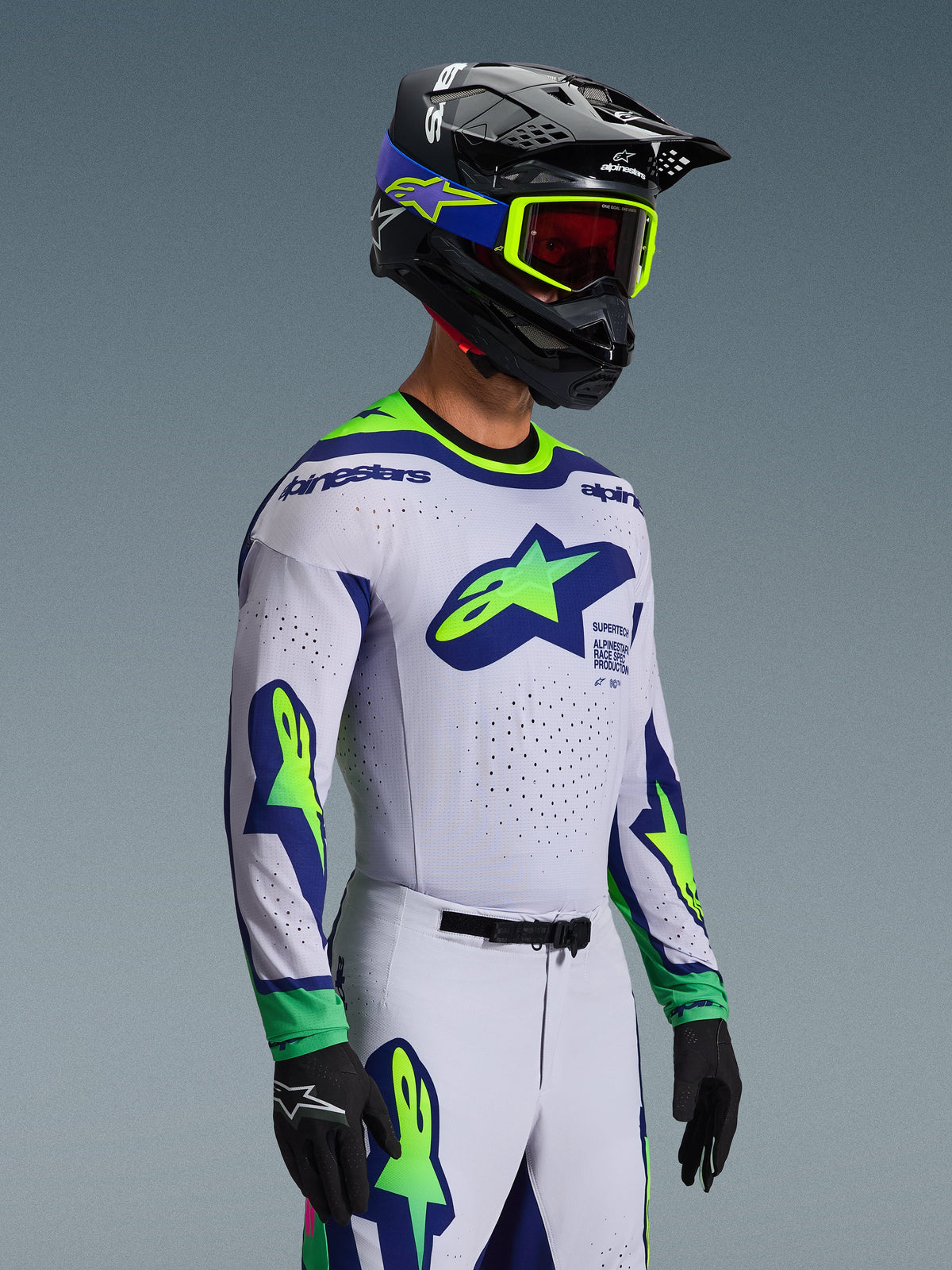 Alpinestars 2026 Supertech Vista Gear Set, Motocross Jersey and Pants, White with Blue and Lime Green accents, worn by a rider with a black helmet and neon green goggles, featuring prominent star logos on the chest and sleeves, athletic pro-level racing fit for off-road performance.