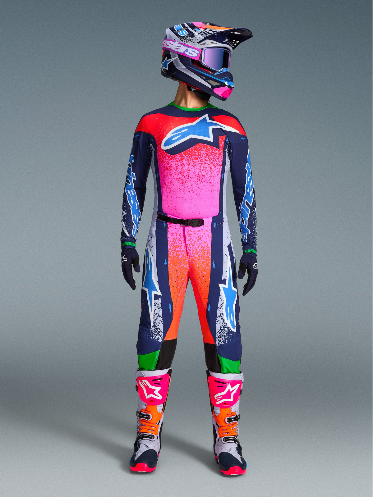 Alpinestars Limited Edition Supertech Records Gear Set, komplett motocross-outfit med marinblå tröja och byxor med livfulla rosa och orangea stänkmönster, matchande hjälm, lila crossglasögon och vita stövlar med rosa detaljer, professionell utrustning med atletisk passform för terrängkörning