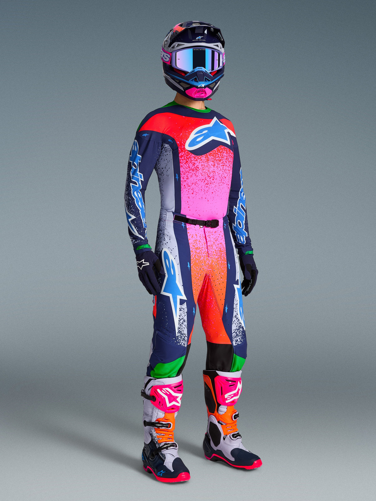 Motocrossförare i Alpinestars Limited Edition Supertech Records Gear Set, med en livfull gradient i rosa, orange och marinblått på tröja och byxor, matchande mönstrad hjälm och goggles, marinblå handskar och koordinerade racingstövlar, komplett professionell outfit för terrängkörning