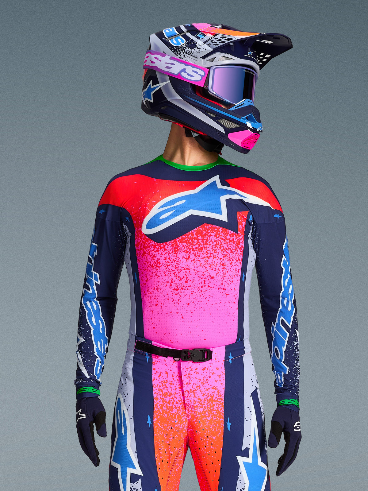 Motocrossförare i Alpinestars Limited Edition Supertech Records Jersey, livfull rosa och marinblå design med orangea stänkmönster och en ljusblå stjärnlogotyp, matchande hjälm och goggles, professionell racingutrustning