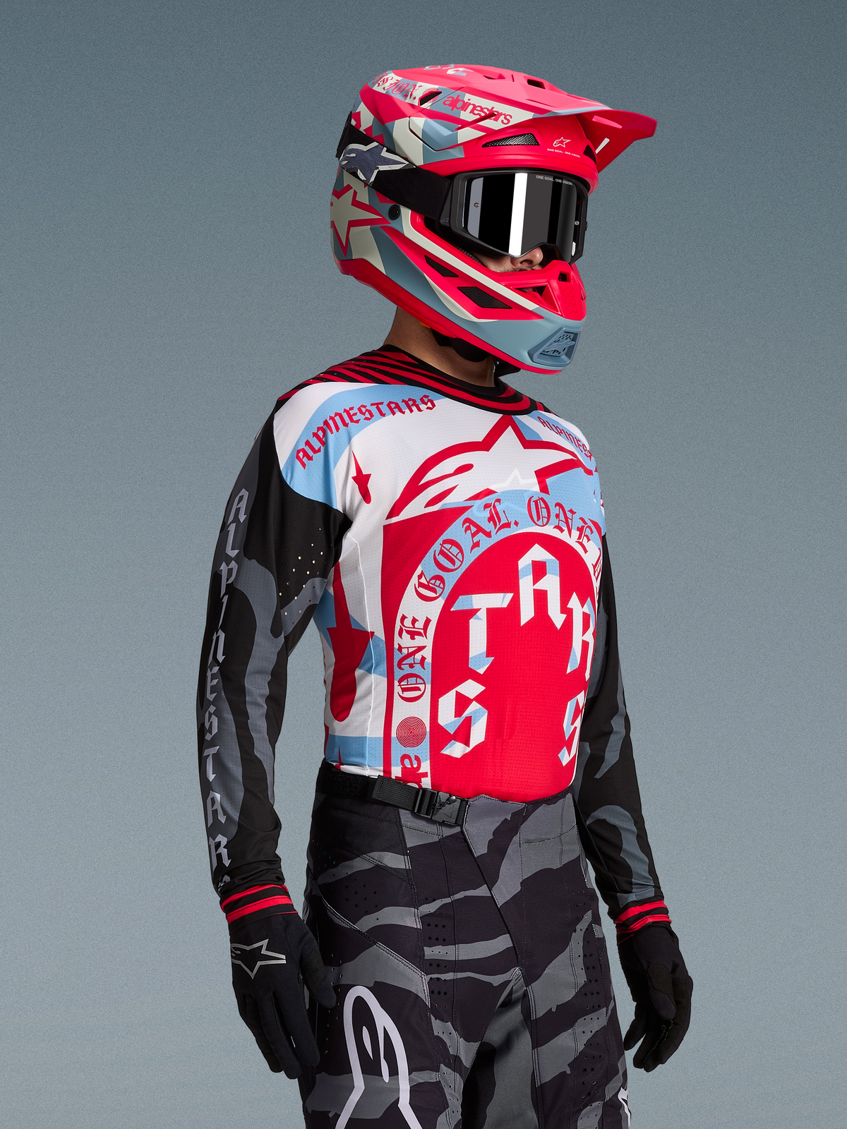 Alpinestars Techstar Beast Coast-tröja i rött, vitt och blått på förare med matchande hjälm och camobyxor.