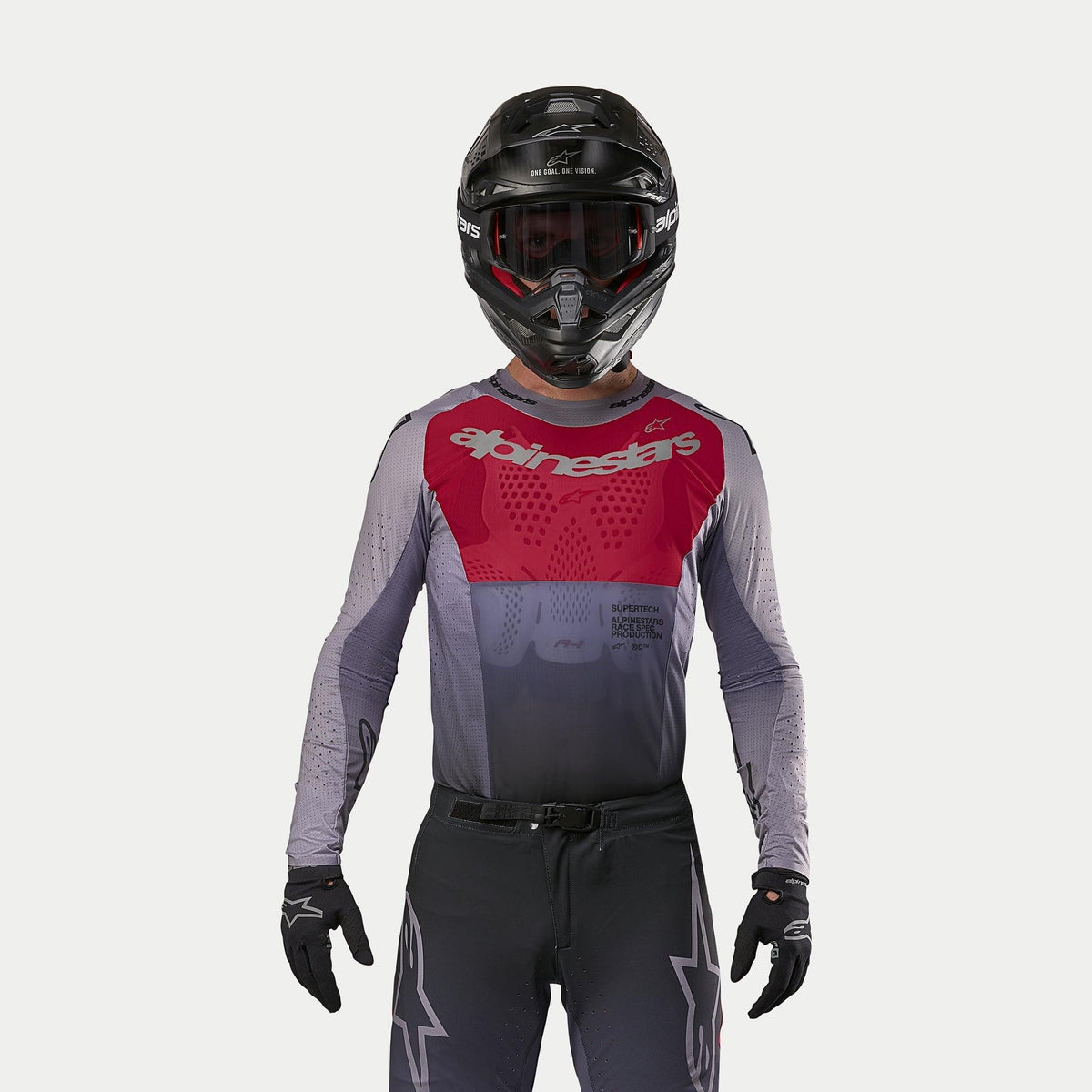 Motocrossförare i Alpinestars 2024 Supertech Dade Jersey i Iron Red Berry, med röd bröstpanel och grå ärmar med logotyper i silver, matchande byxor, svart hjälm och svarta handskar, professionell utrustning för terrängkörning