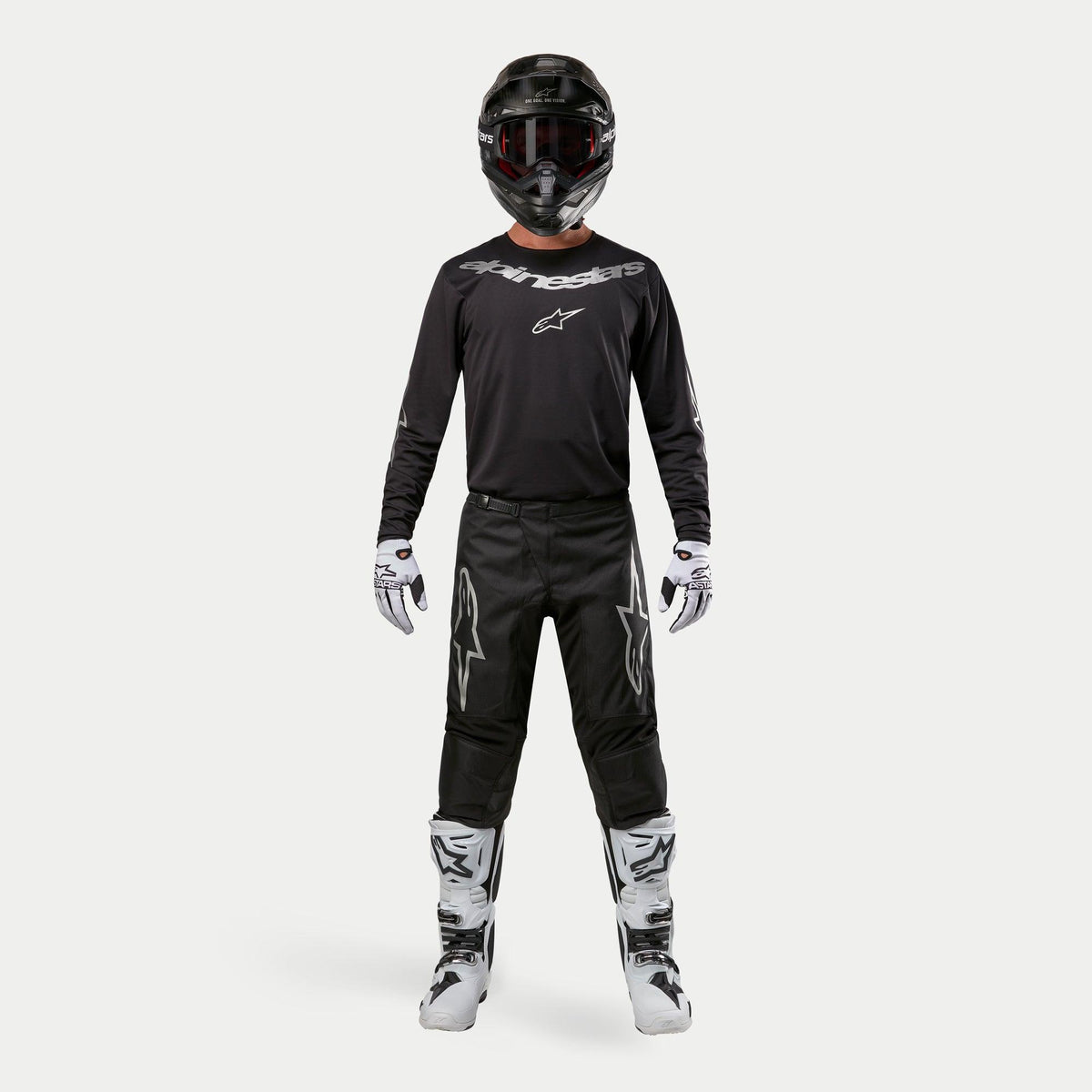 Motocrossförare i komplett racingutrustning, Alpinestars 2024 Fluid Graphite-tröja i Black Silver, svarta byxor med silverfärgade stjärnlogotyper, svart hjälm med röda goggles, vita och svarta stövlar, vita och svarta handskar, koordinerad motocross-outfit